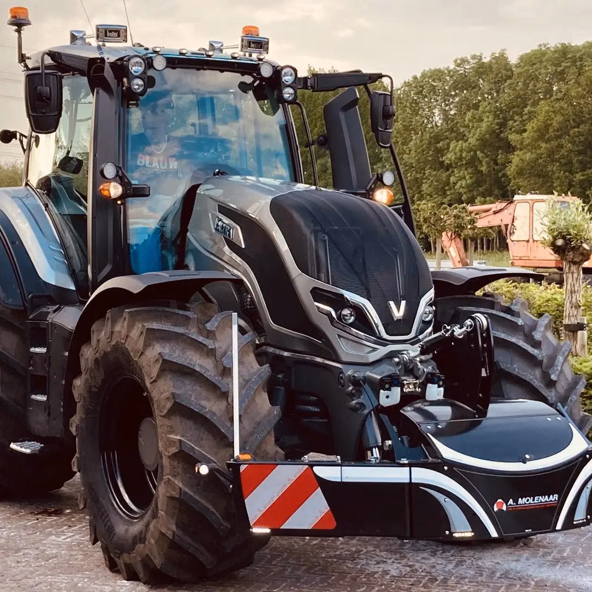 A black tractor with large tires is equipped with a front weight bumper featuring red and white safety stripes.