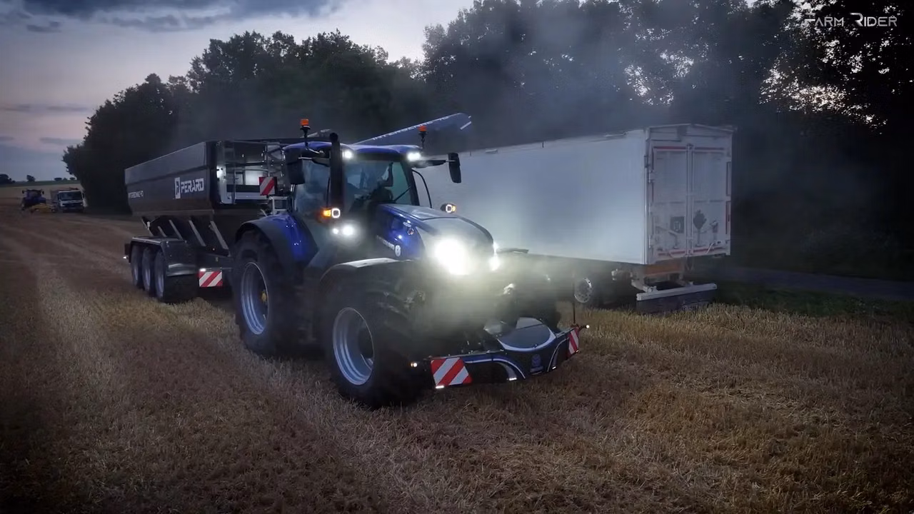 A blue tractor with headlights on is fitted with a front weight bumper and is working in a harvested field at dusk