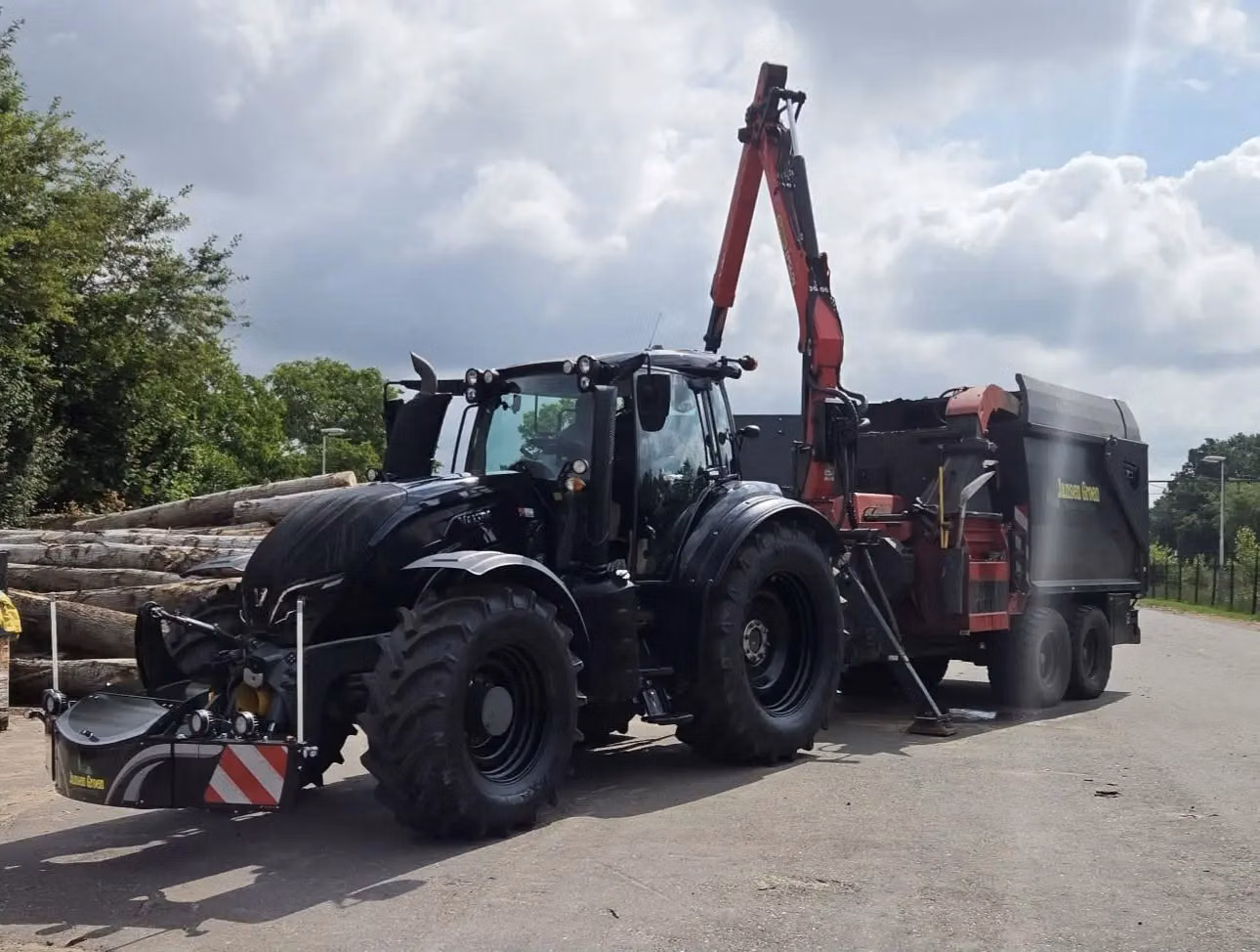 Black tractor with a front weight bumper and LED lights attached, working beside a log loader and trailer