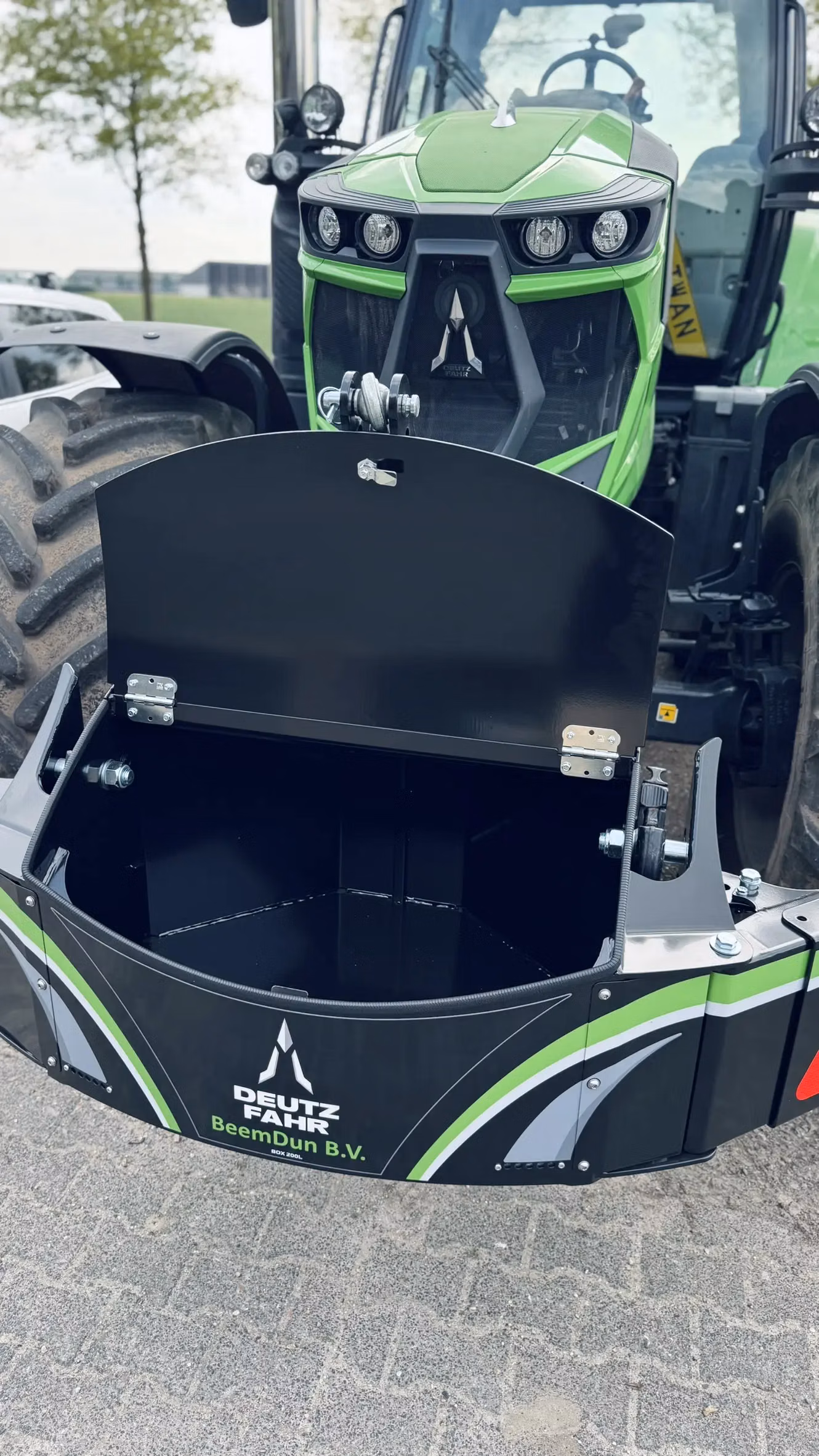 A green tractor with a black front weight bumper featuring an open storage compartment and Deutz-Fahr branding