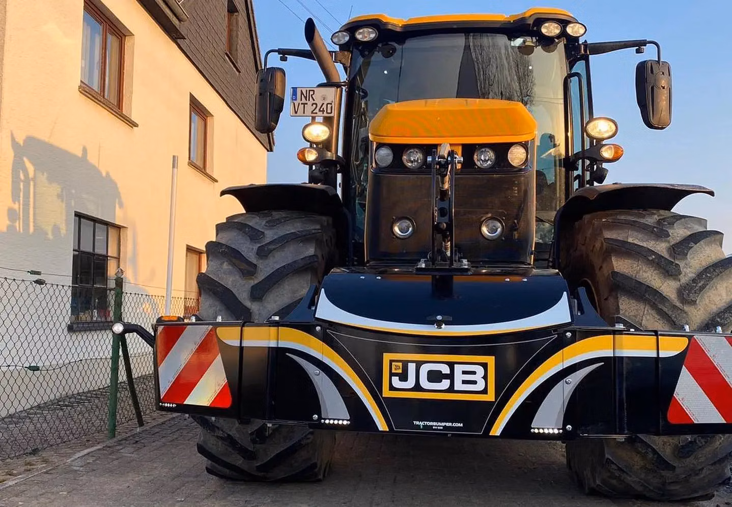 A large tractor with rugged tires is fitted with a black and yellow front weight bumper displaying the JCB logo.