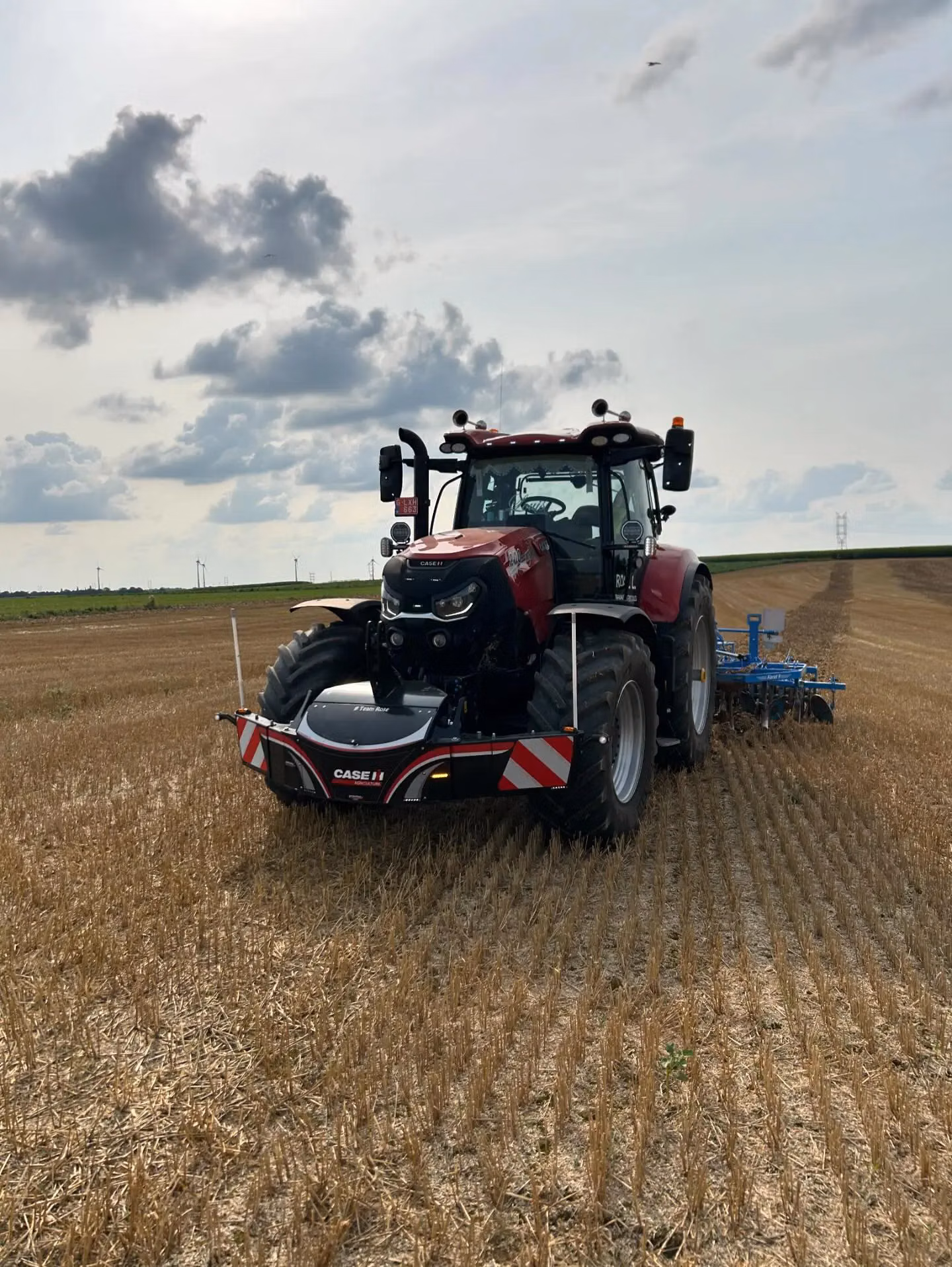 Red tractor with a front weight bumper and reflective stripes working in a harvested field under a cloudy sky