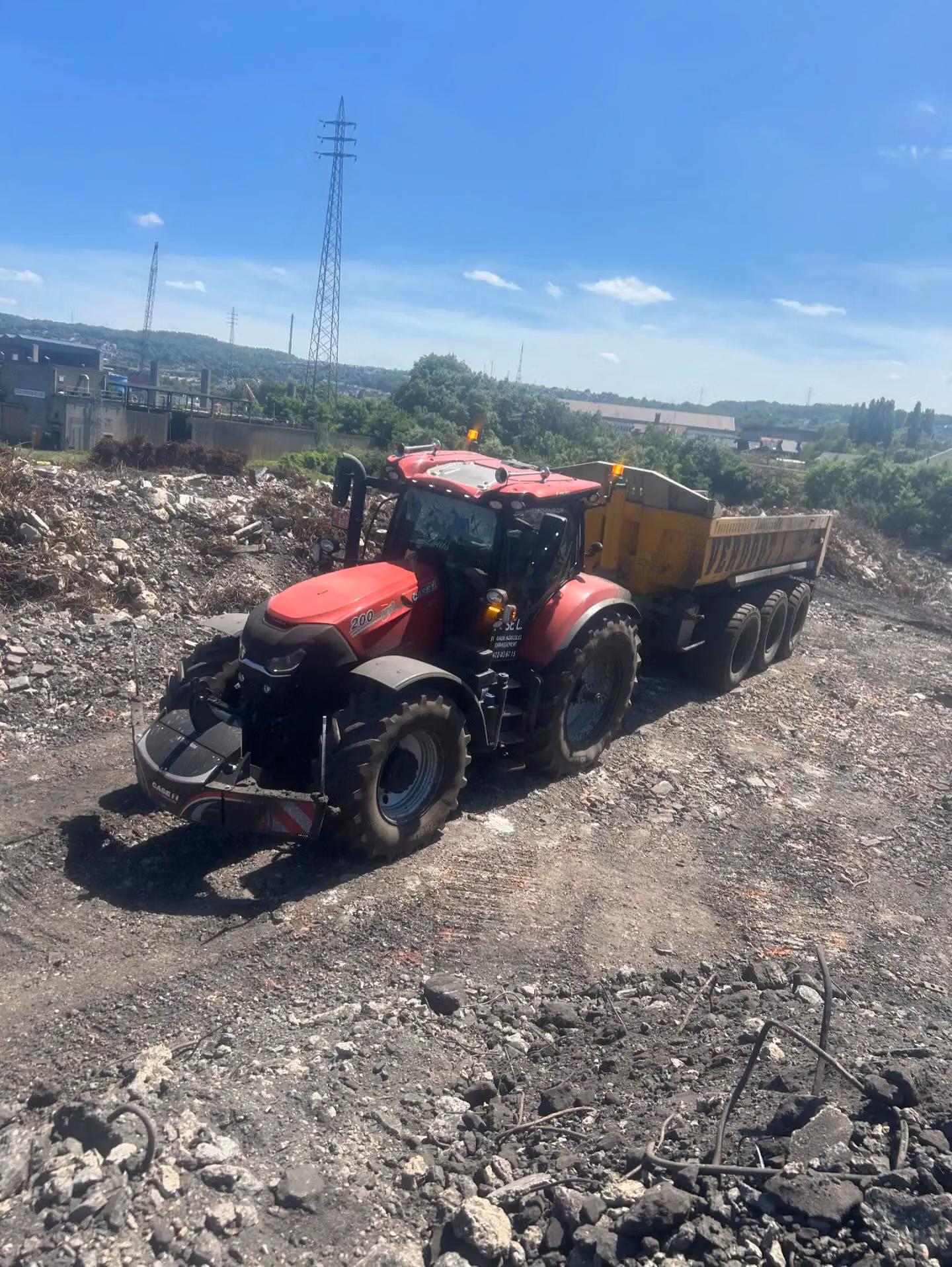 Red tractor with a front weight bumper attached, pulling a large yellow trailer on a rocky dirt surface