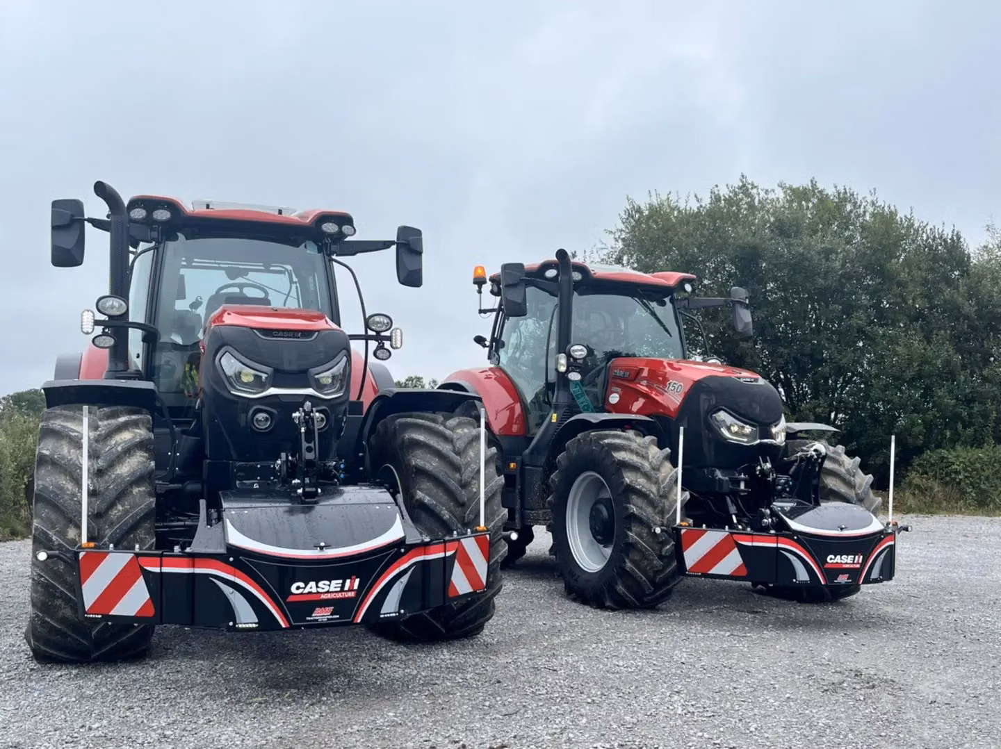 Two red tractors fitted with black Case IH front weight bumpers on a gravel surface with trees in the background