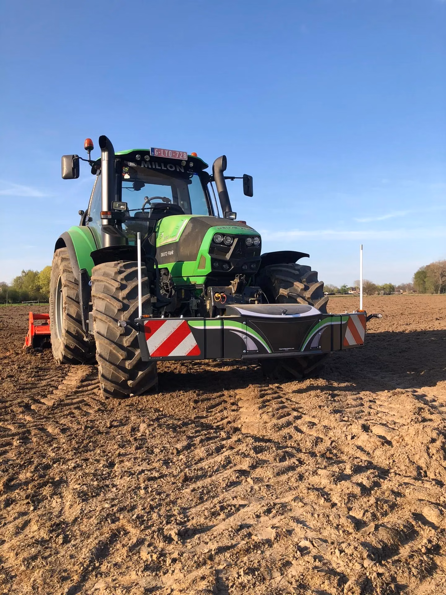 A green tractor in a field equipped with a front weight bumper featuring reflective red and white stripes