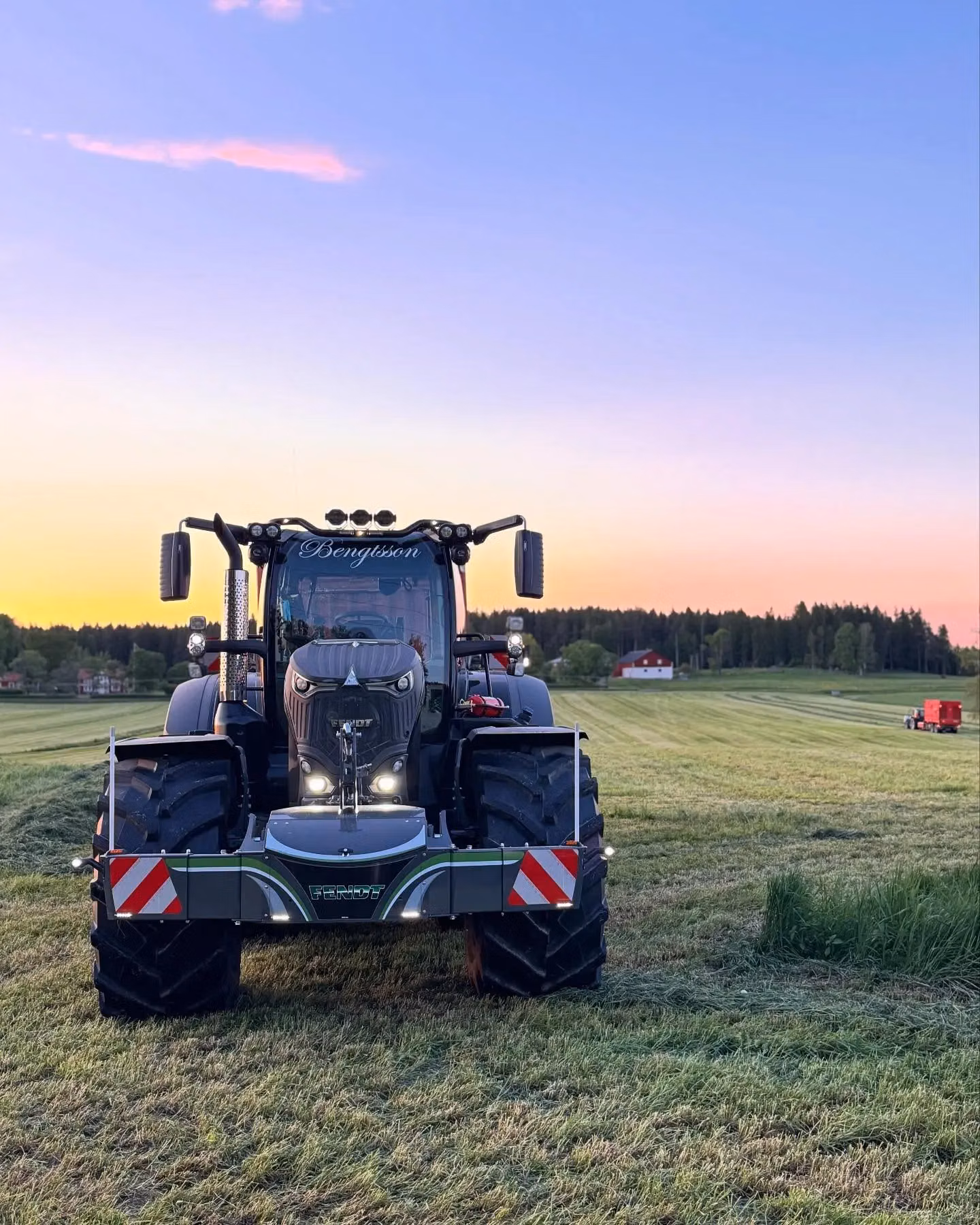 A tractor fitted with a front weight bumper stands on a grassy field at sunset with trees and a building in the background