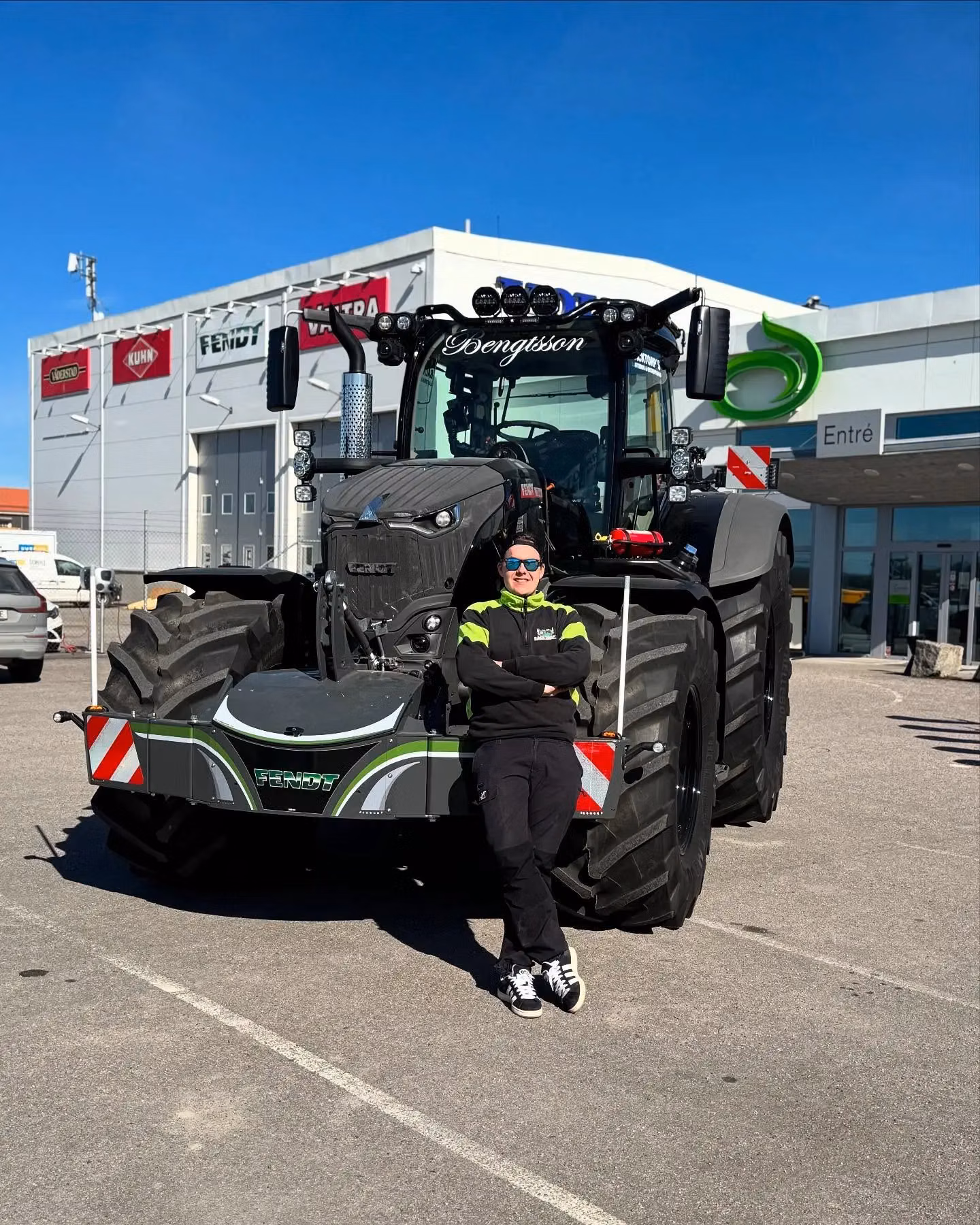 Person in dark clothing leans against a tractor equipped with a front weight bumper labeled Fendt in a parking lot