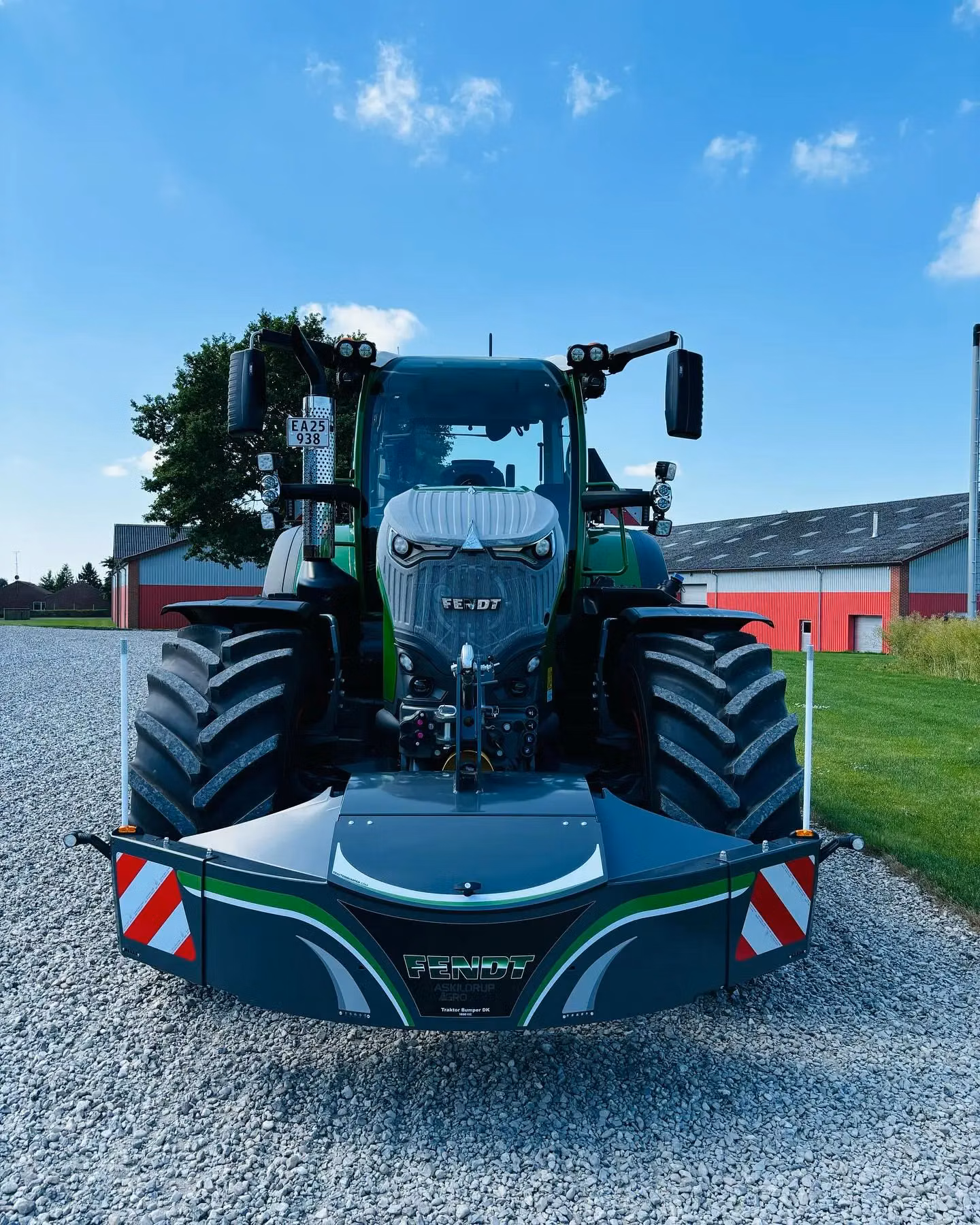 A green tractor with a mounted front weight bumper featuring reflective stripes and LED lights, parked on gravel