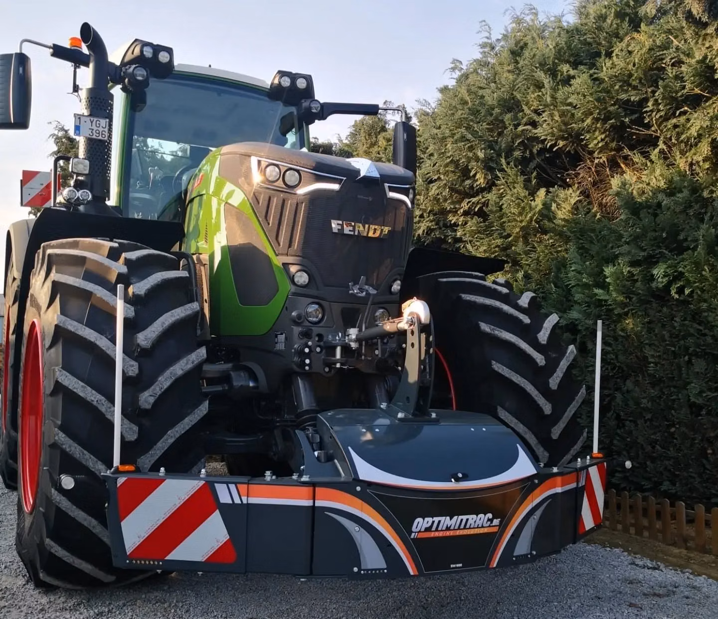 A green tractor with a large front weight bumper featuring reflective red and white stripes and Optimitrac branding
