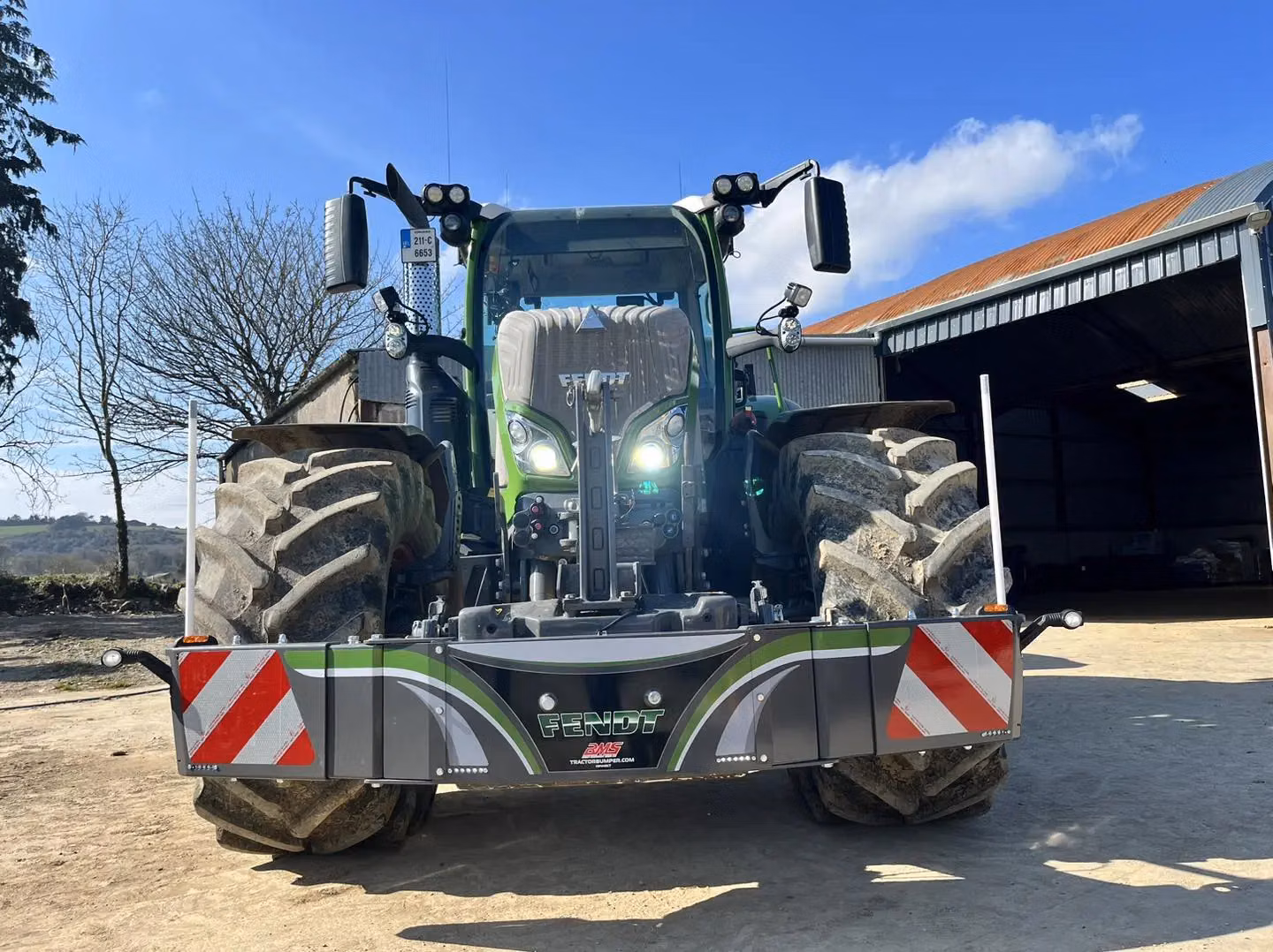 A green tractor fitted with a wide front weight bumper displaying reflective stripes and Fendt branding