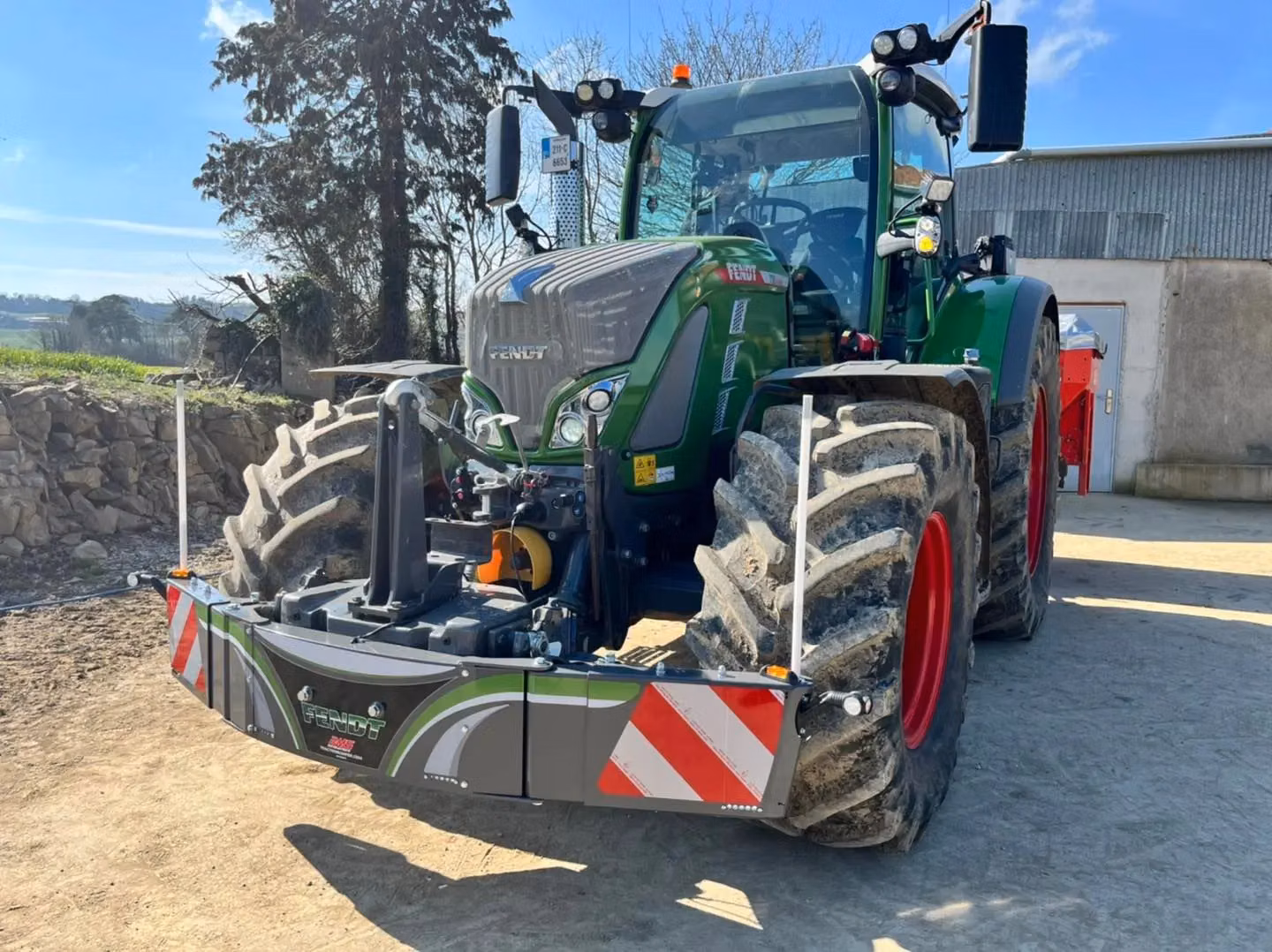 A tractor with a front weight bumper featuring LED lights and red and white reflective stripes on a dirt surface