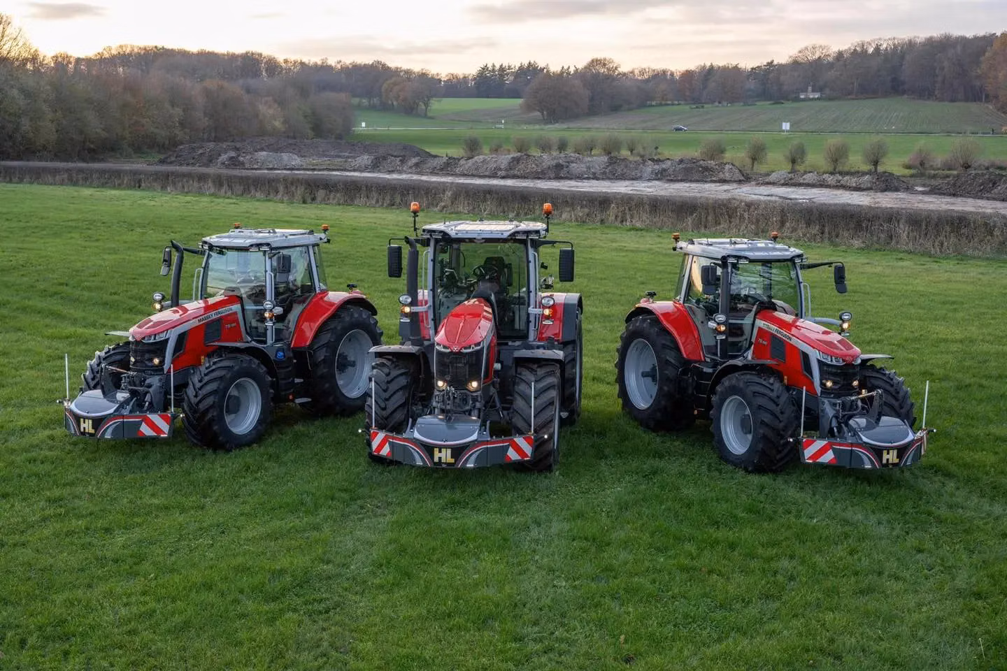 Three red tractors with front weight bumpers are parked on grass with a rural landscape in the background
