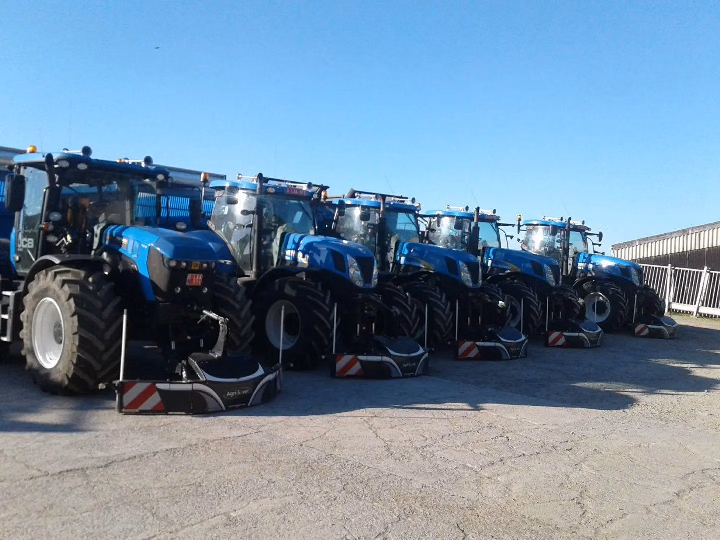 Five blue tractors parked in a row, each equipped with a large black and white front weight bumper