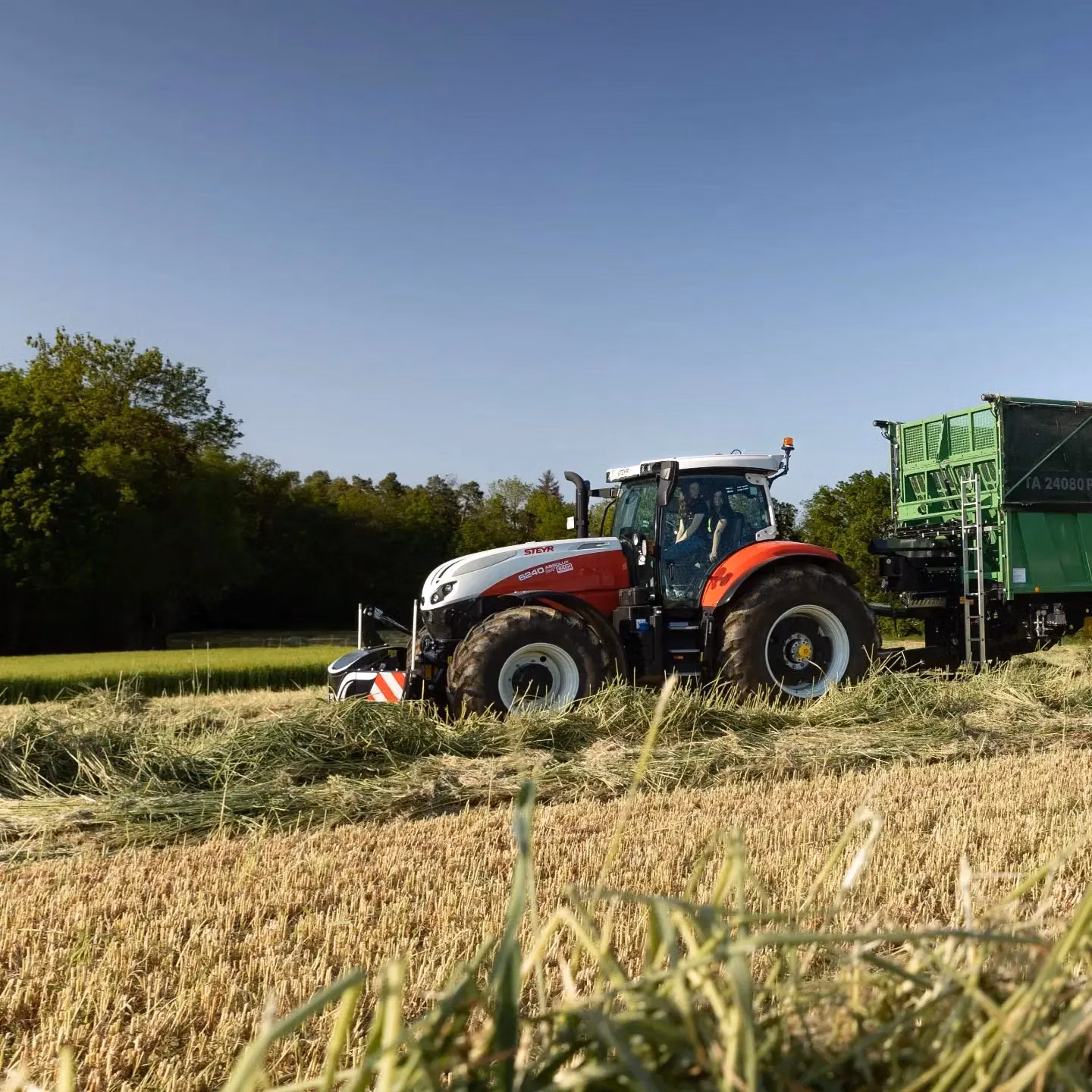 A tractor with a front weight bumper attached works in a field, pulling a green trailer on a sunny day