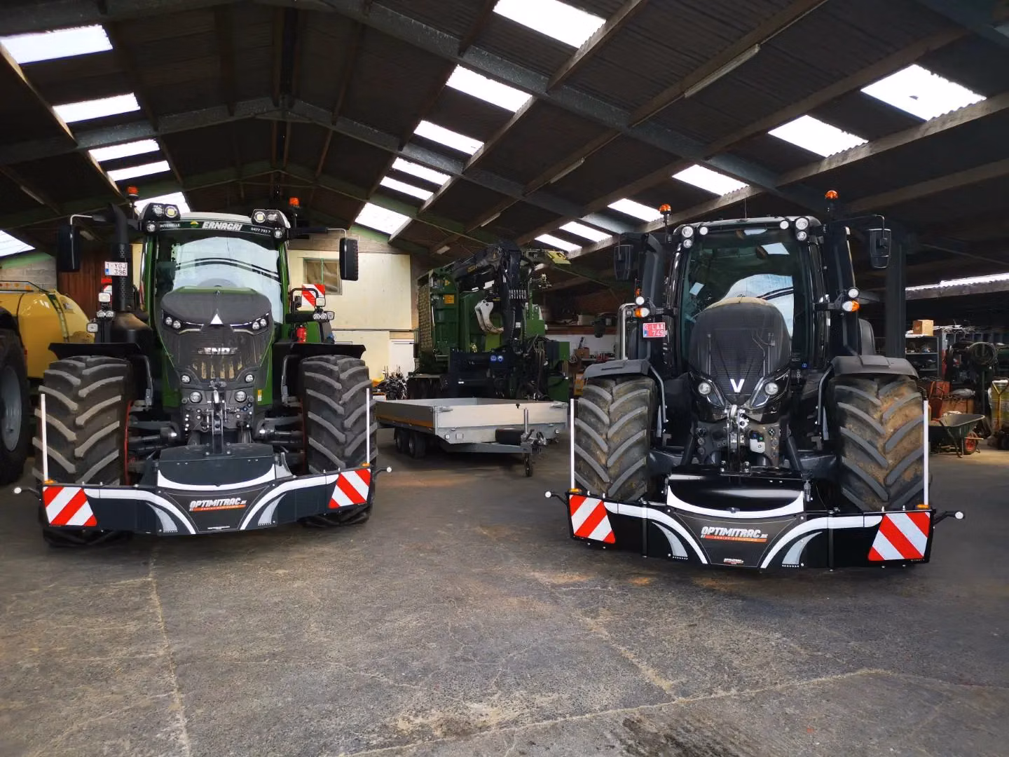Two tractors indoors equipped with front weight bumpers featuring red and white safety stripes and LED lights