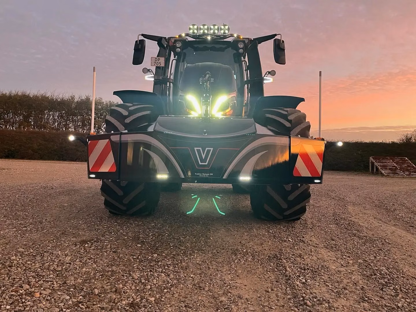 Large tractor with a front weight bumper featuring LED lights, reflectors, and striping, photographed at sunset