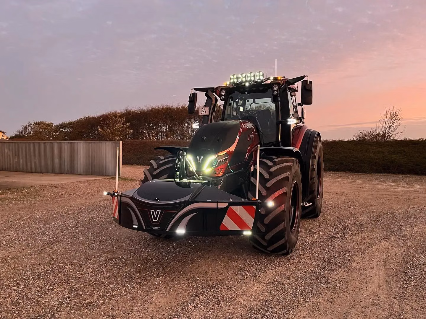 A tractor with a mounted front weight bumper that features LED lights and reflective safety markings.