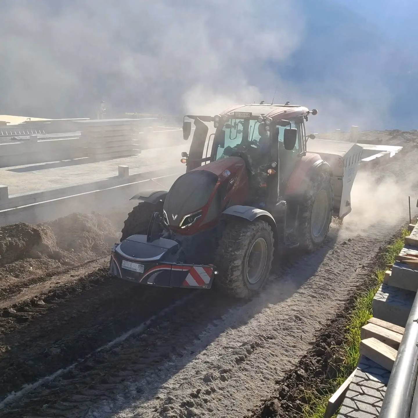 Red tractor with a front weight bumper and LED light box driving on a dusty dirt track at a construction site