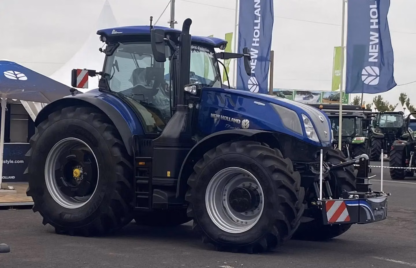 Blue tractor on display with a front weight bumper attached and flags in the background