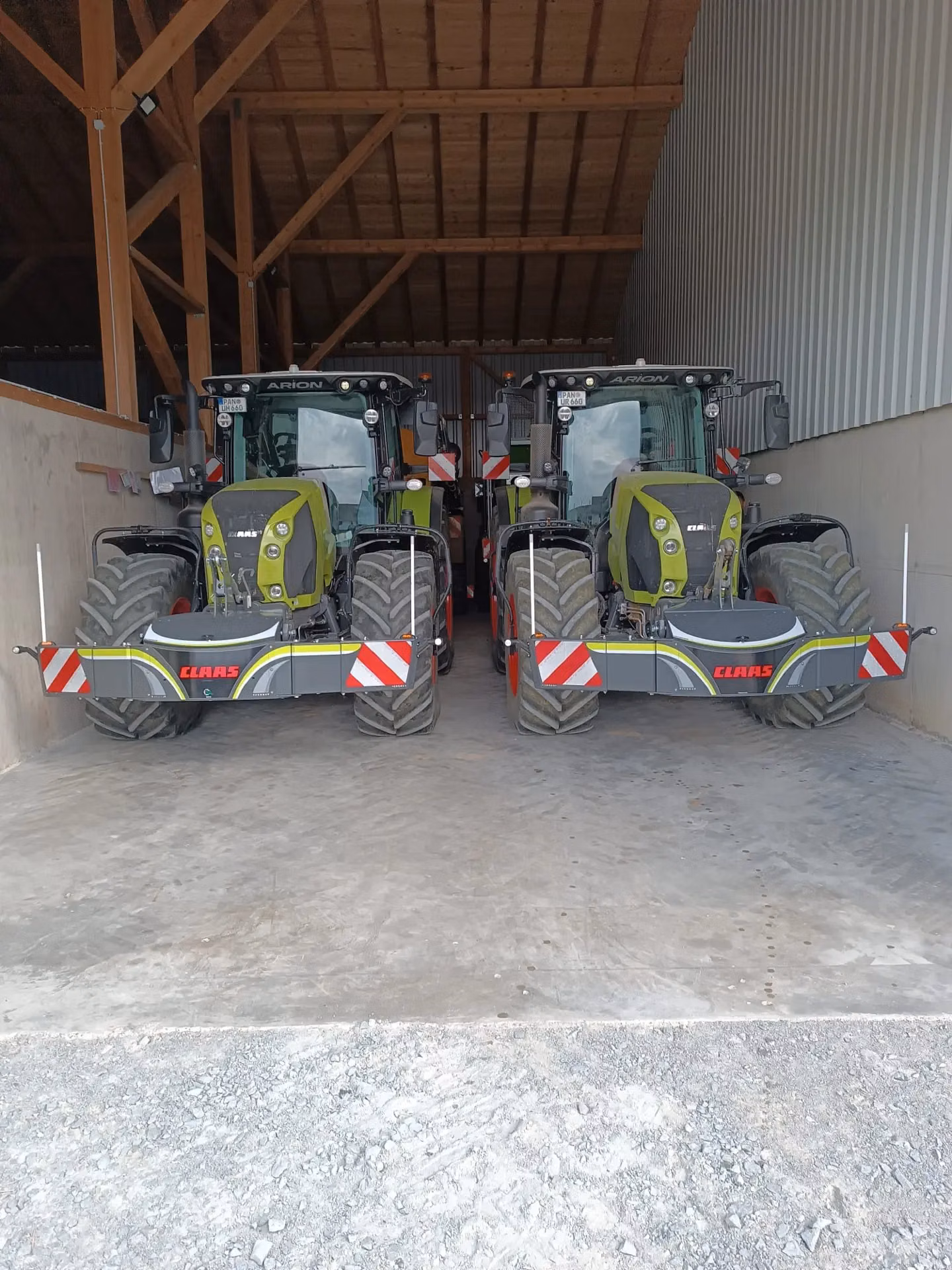 Two green tractors with front weight bumpers displaying reflective stripes parked side by side in a barn