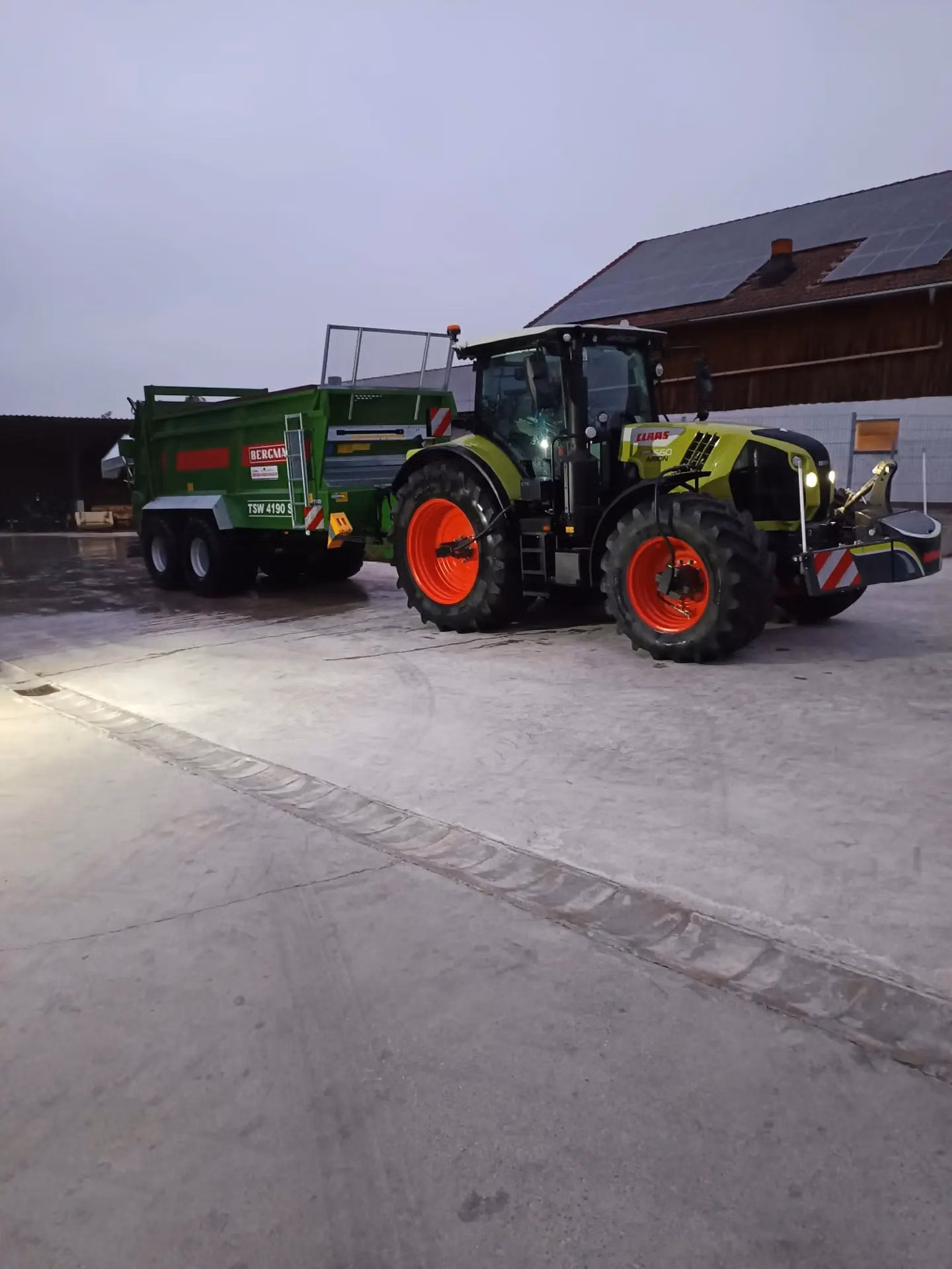Green tractor with a front weight bumper and LED lights is parked outdoors, attached to a green trailer