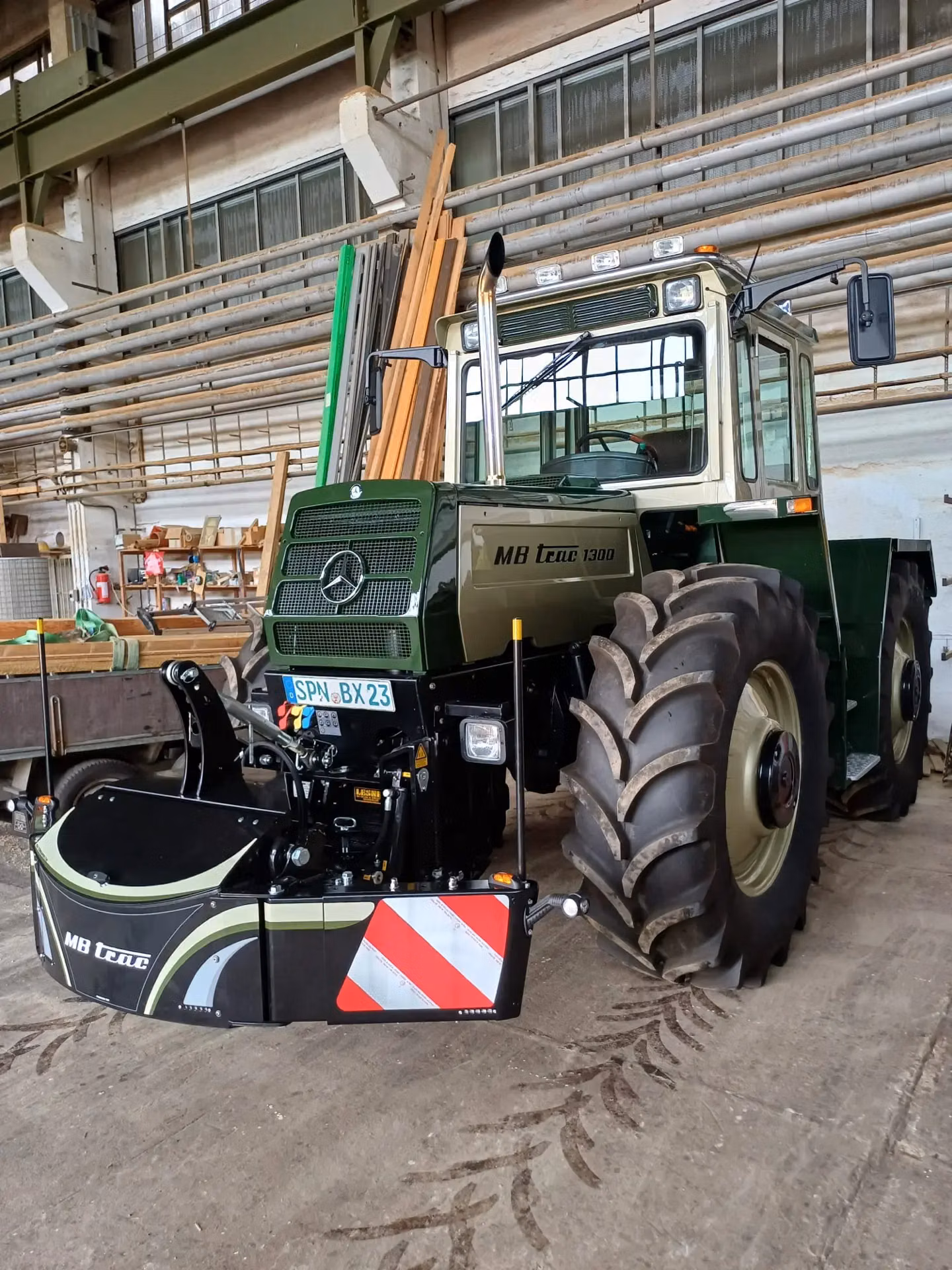 A green tractor with a large front weight bumper featuring red and white safety stripes in an indoor workshop
