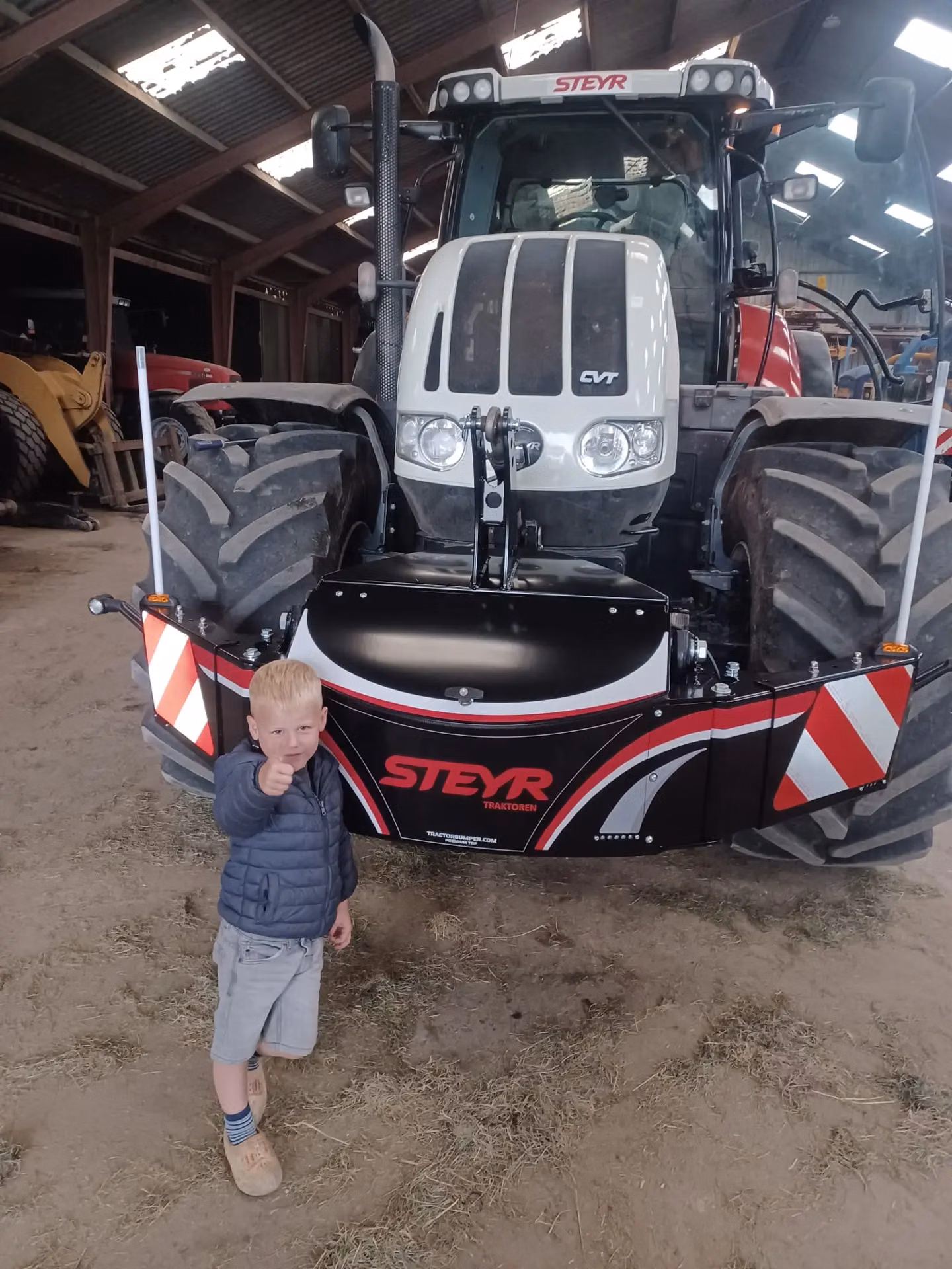 A child stands in front of a Steyr tractor fitted with a front weight bumper featuring reflective strips and LED lights