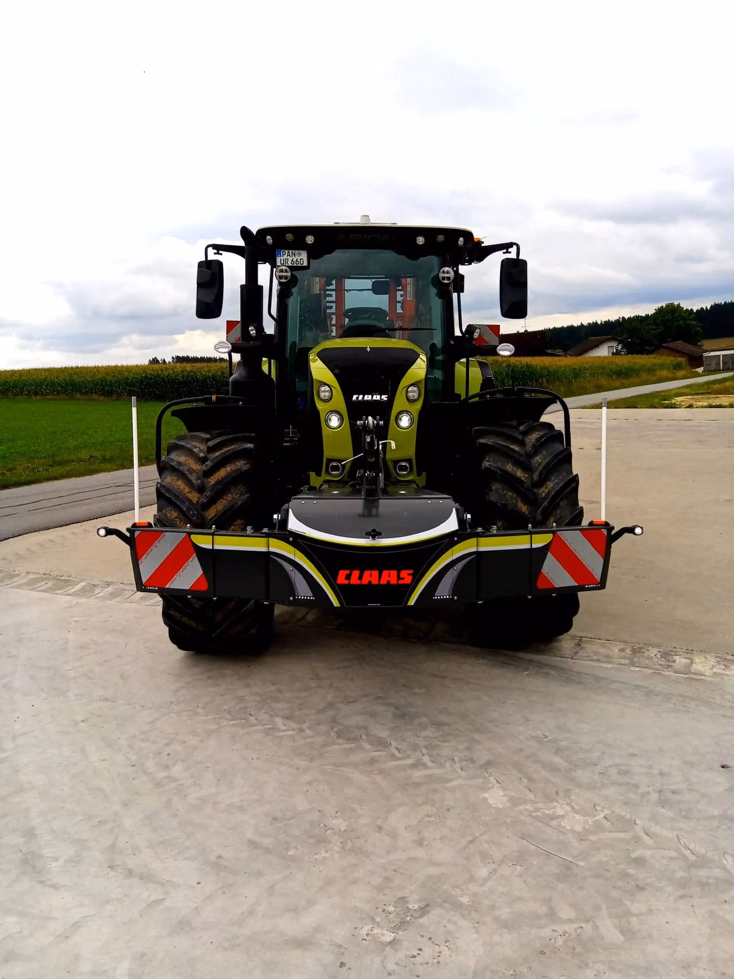 A tractor fitted with a front weight bumper featuring reflective red and white stripes and the CLAAS logo