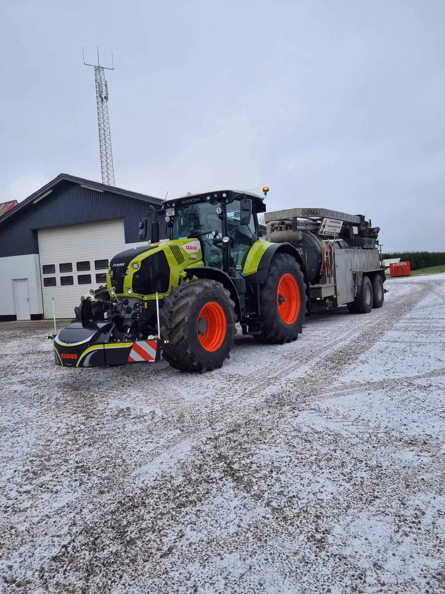 A green tractor with a CLAAS-branded front weight bumper is parked on gravel with a large trailer attached