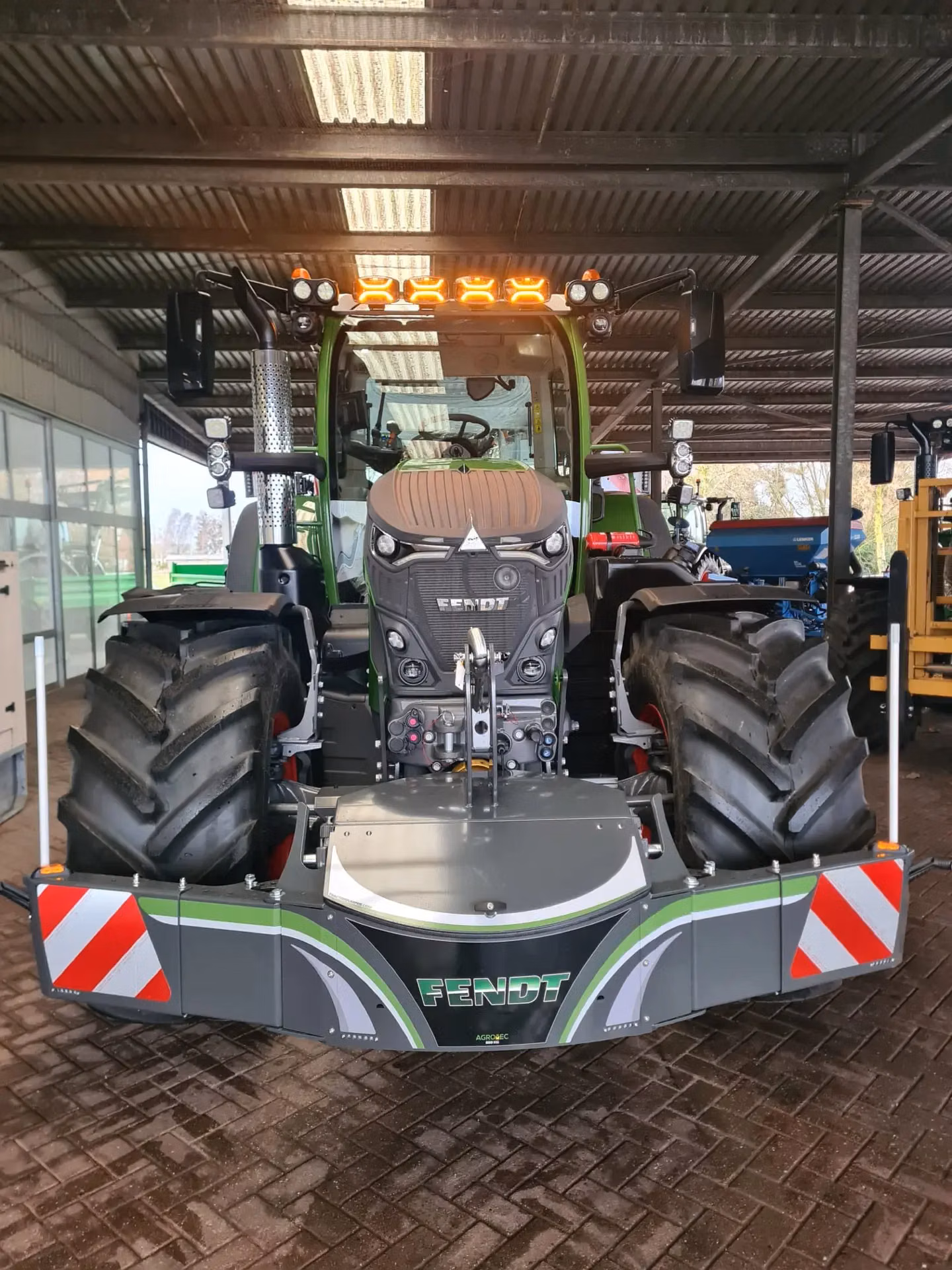 Tractor with a Fendt front weight bumper featuring integrated lights and red and white safety stripes, parked indoors