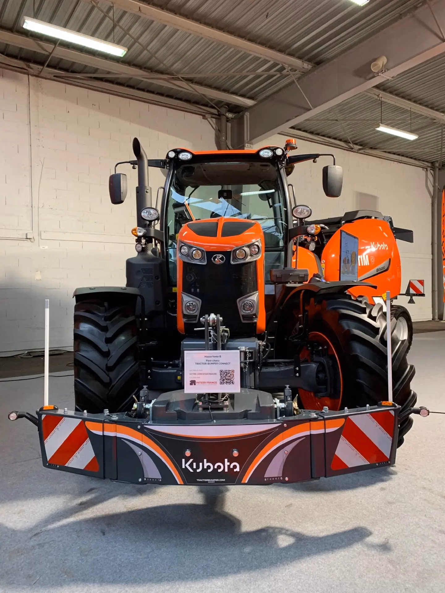 Front view of an orange tractor indoors with a Kubota-branded front weight bumper attached.