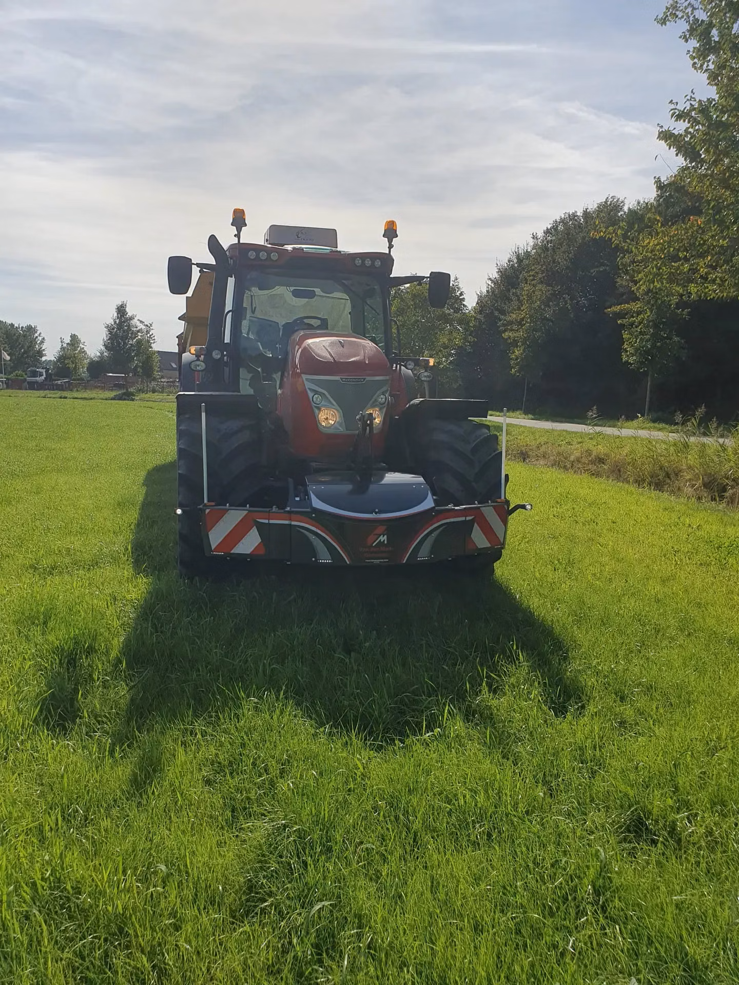 A red tractor fitted with a front weight bumper and LED lights is parked on green grass facing forward