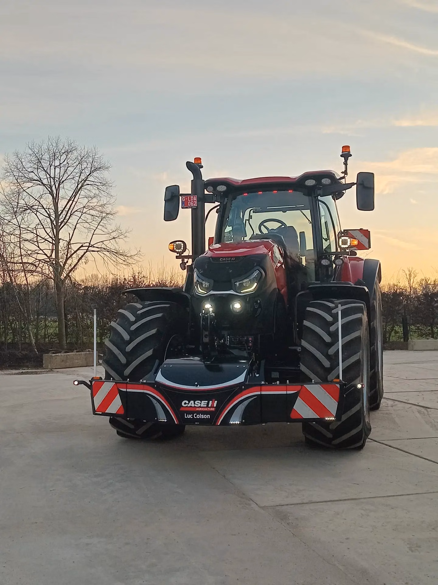 Red tractor with large front wheels, fitted with a Case IH branded front weight bumper on a concrete surface at sunset