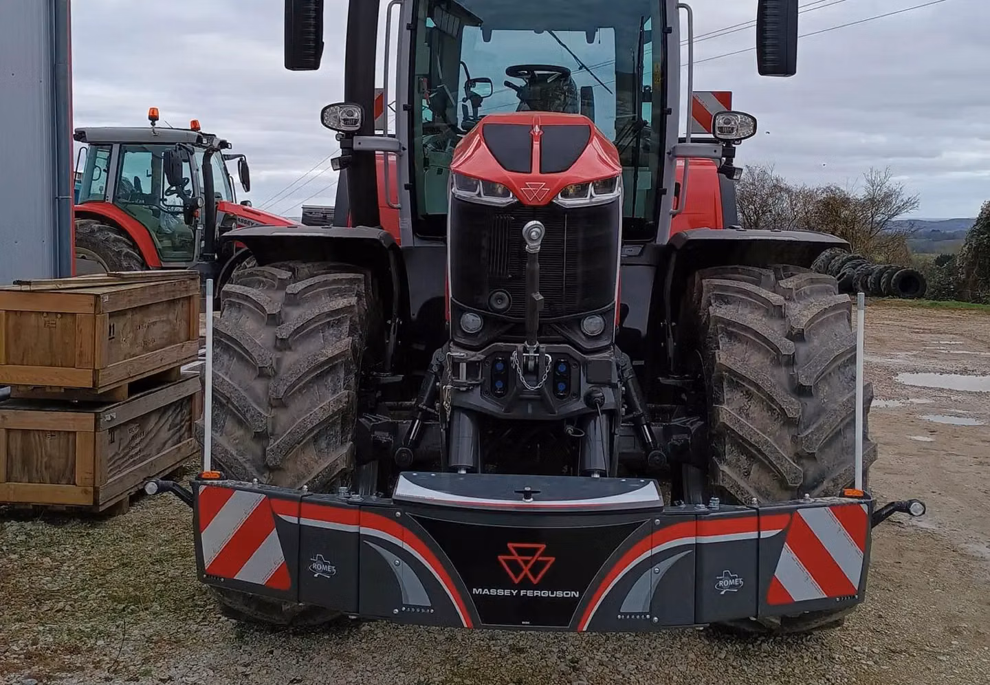 Front view of a red tractor with a Massey Ferguson branded front weight bumper in a farmyard setting