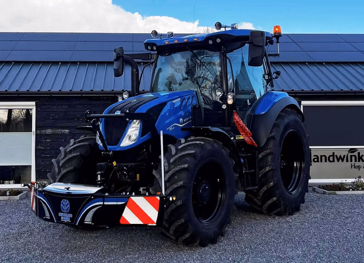 Blue tractor with a large front weight bumper featuring reflective red and white stripes and logo detailing