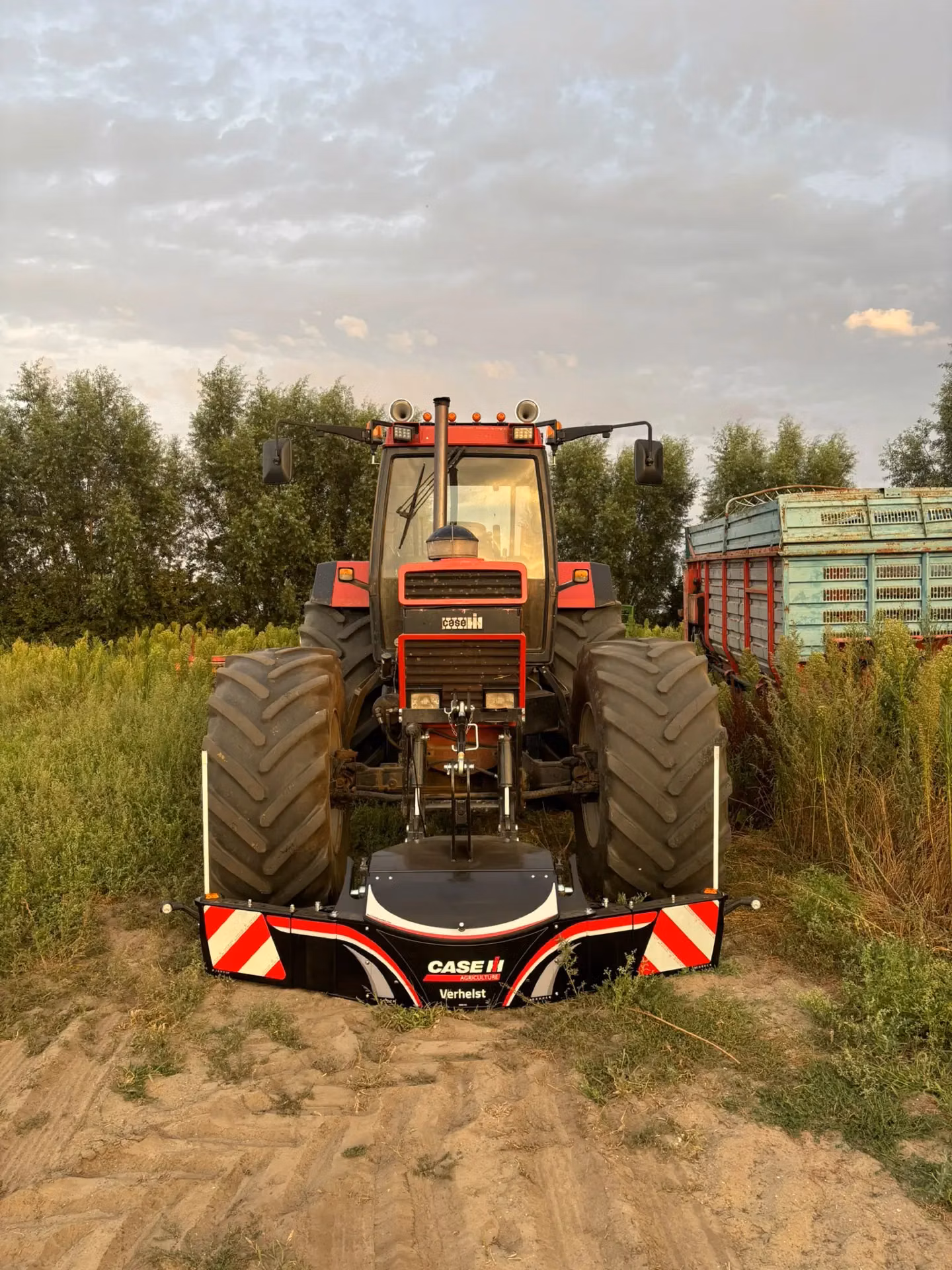 A red tractor with large rear tires is equipped with a Case IH front weight bumper on a dirt path in a field