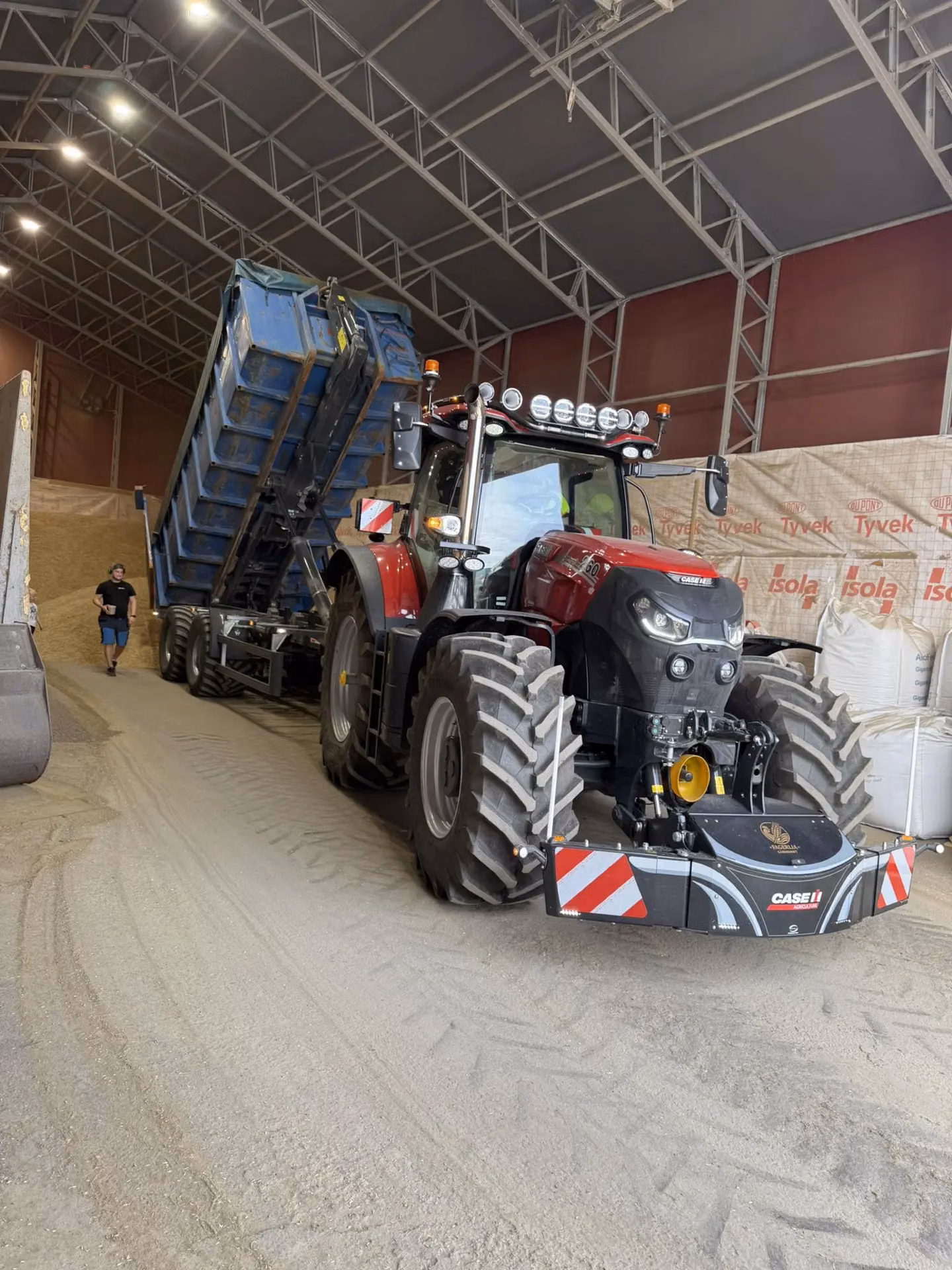 Red tractor indoors with a front weight bumper featuring lights and reflective stripes, trailer tipping in background