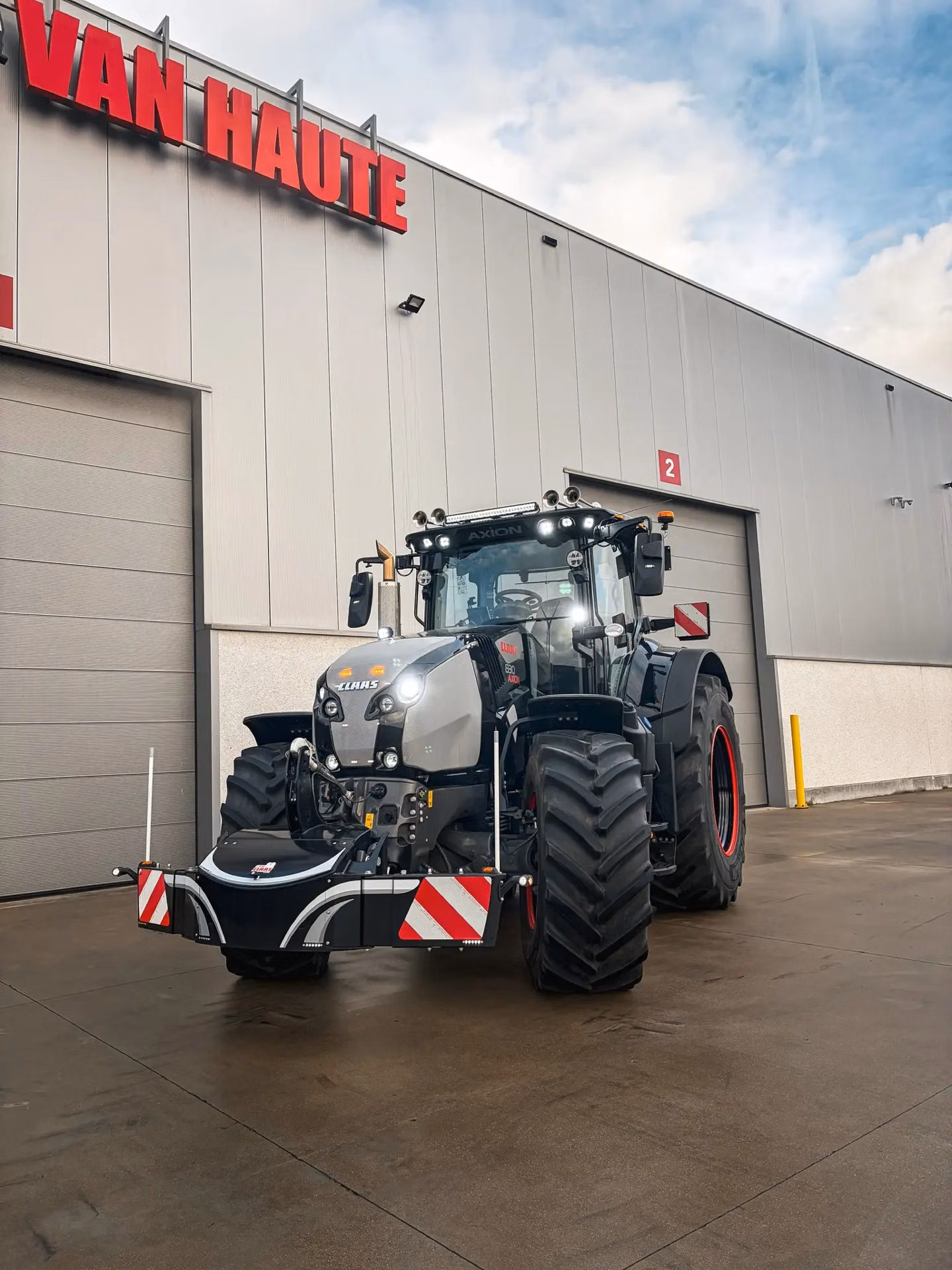 A tractor with a front weight bumper and red-white hazard markings parked outside a commercial building