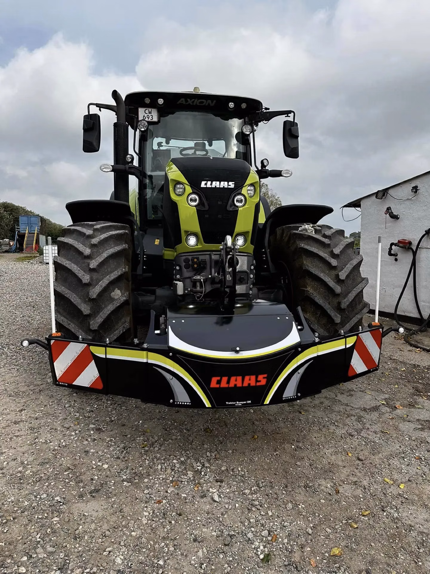 Claas tractor fitted with a front weight bumper featuring reflective stripes and Claas branding, parked on gravel