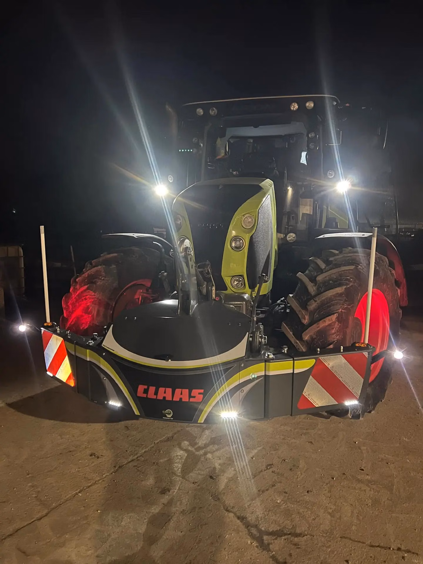 Tractor at night with headlights on, featuring a CLAAS-branded front weight bumper with reflective panels