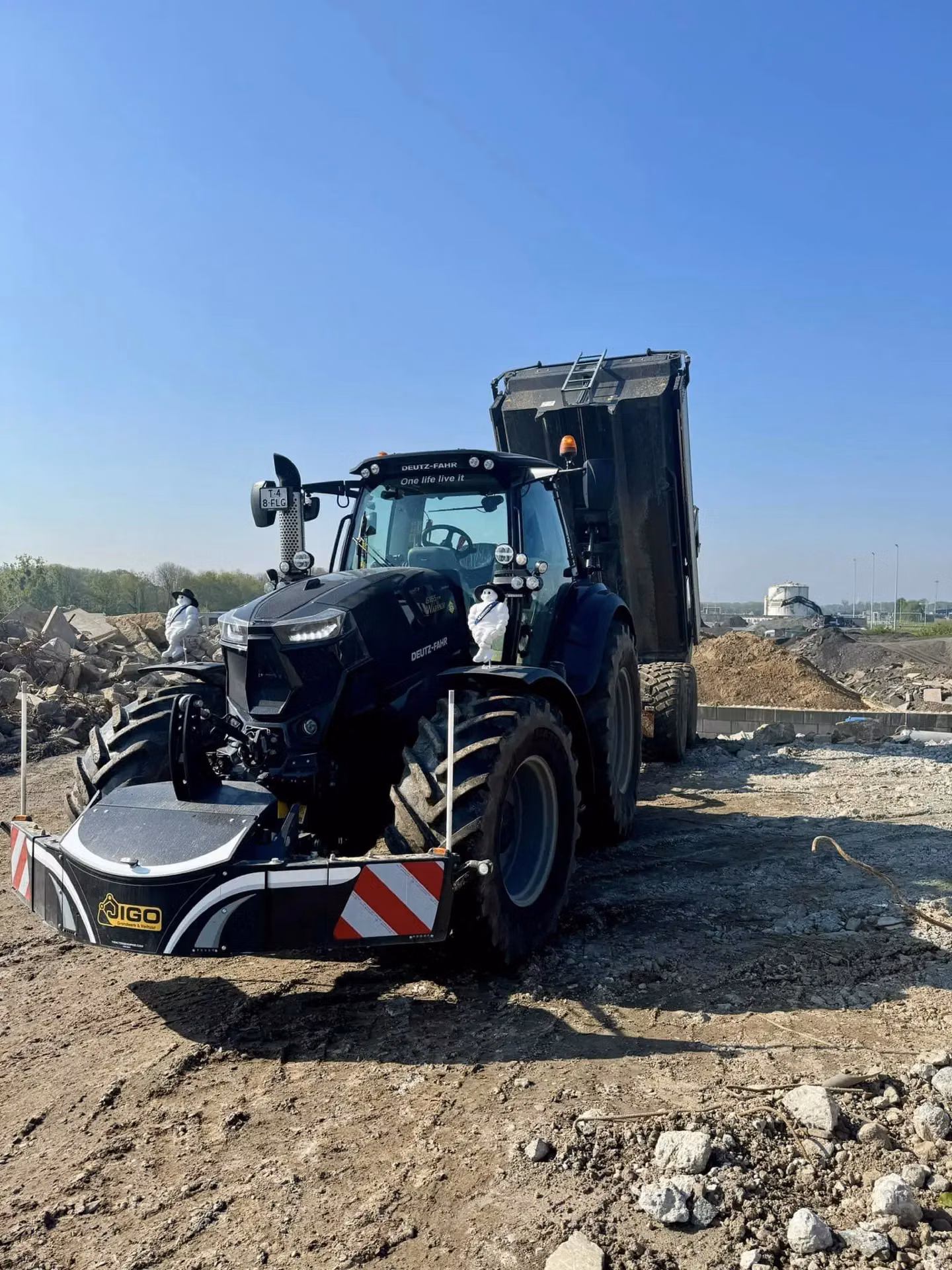 A tractor with a front weight bumper and striped reflectors is parked on a construction site near a dump truck