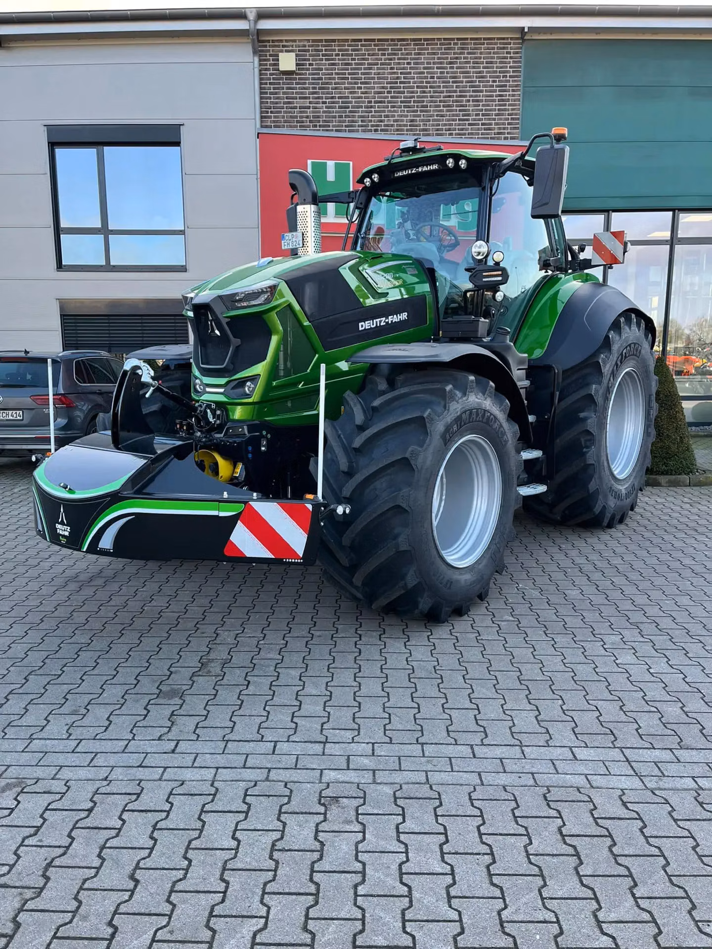 Green tractor with large front weight bumper attached, parked on paved area in front of a building