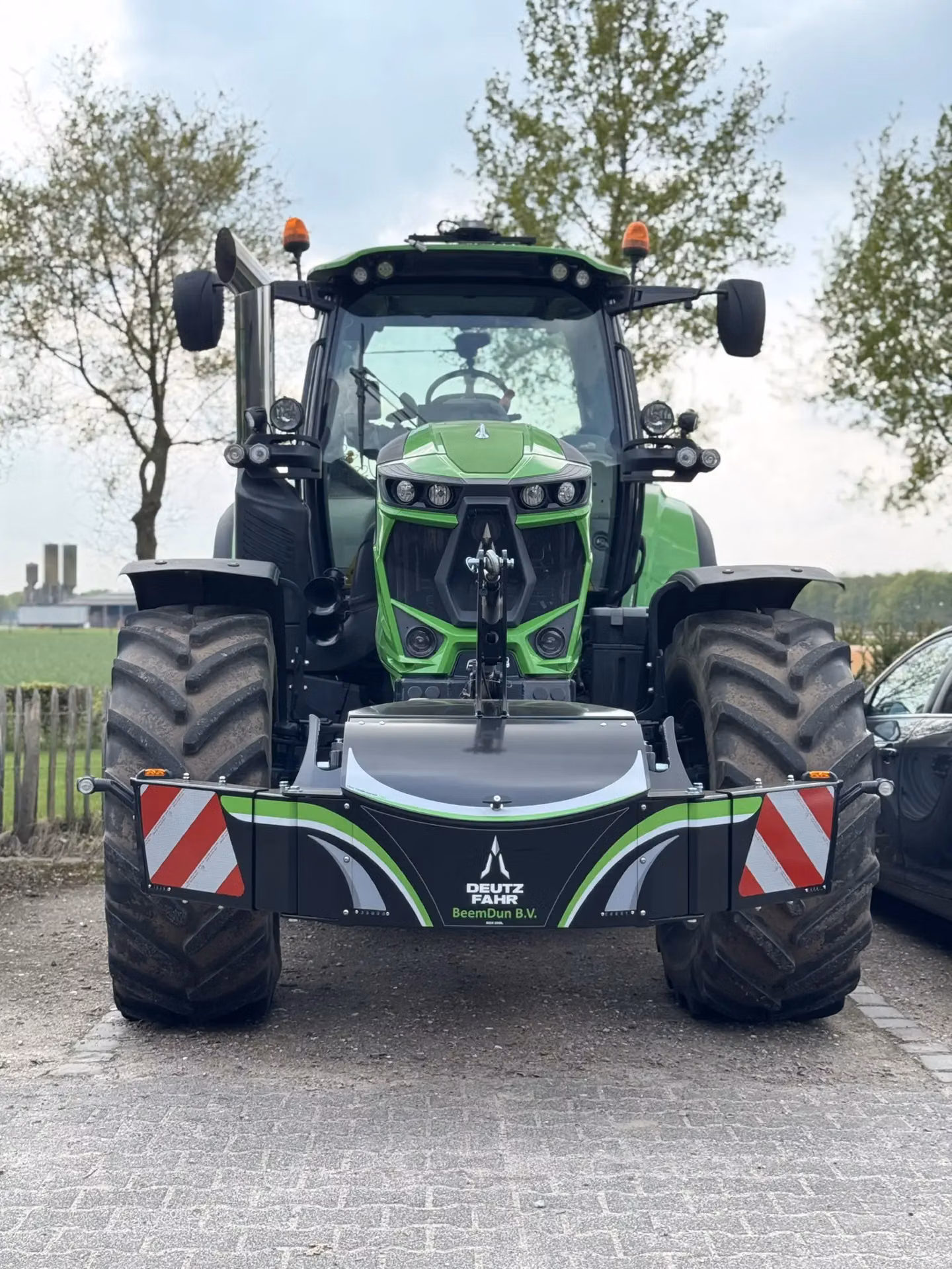 A green tractor with large tires fitted with a Deutz Fahr BeemDun B.V. front weight bumper and warning reflectors