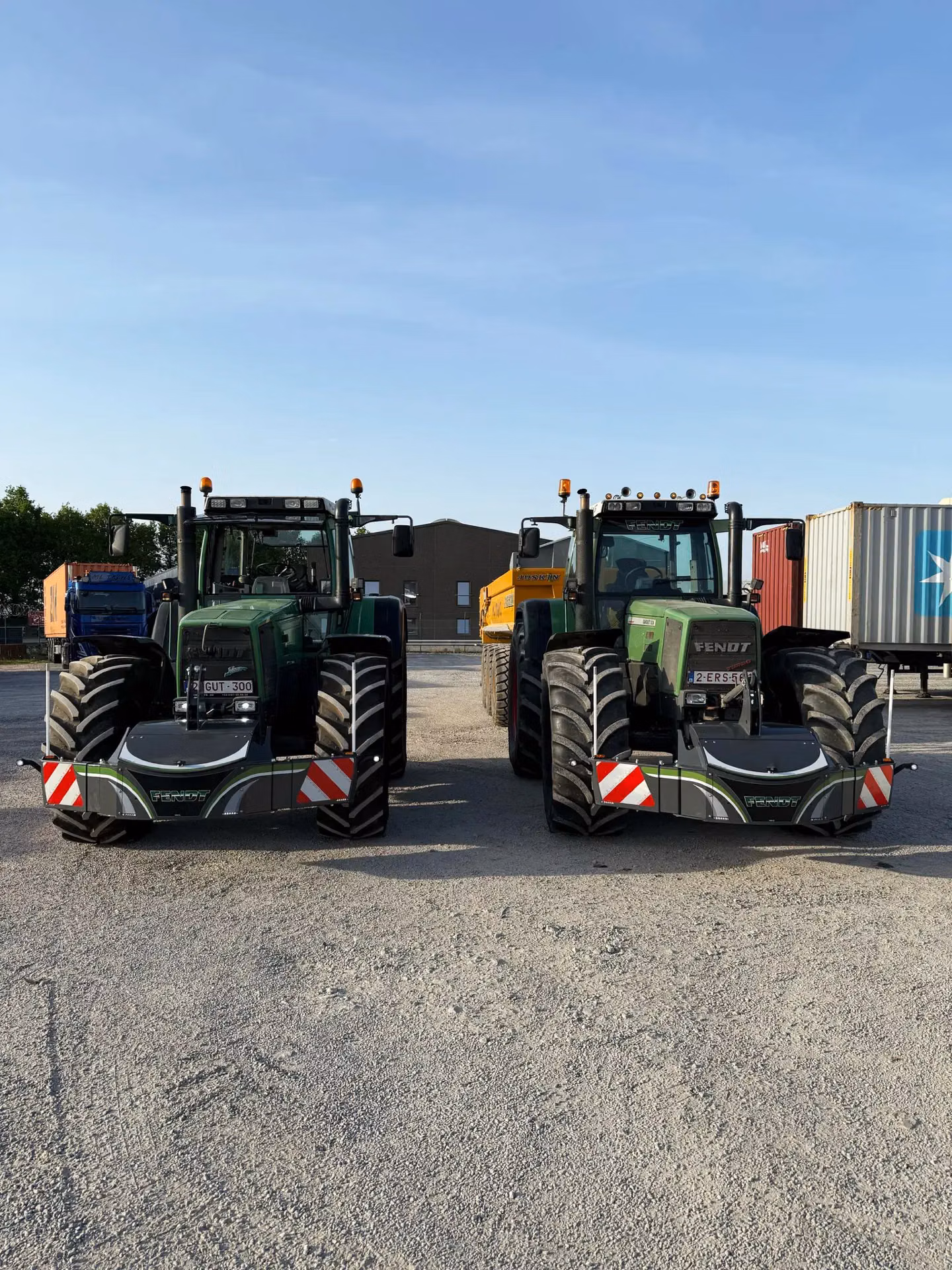 Two green tractors with large front weight bumpers and red-white warning stripes parked side by side outdoors
