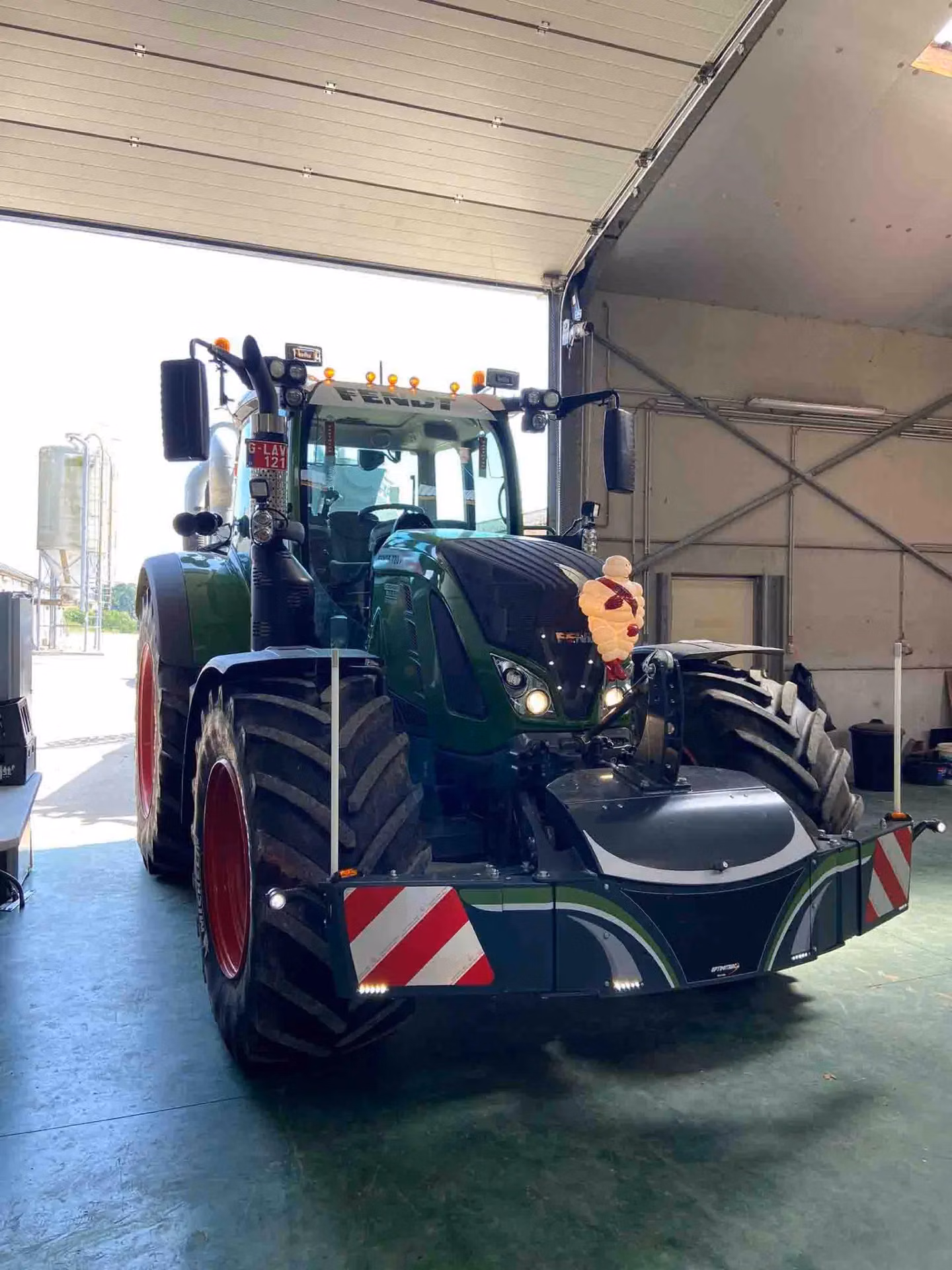 Large tractor in a garage fitted with a front weight bumper featuring red and white reflective stripes