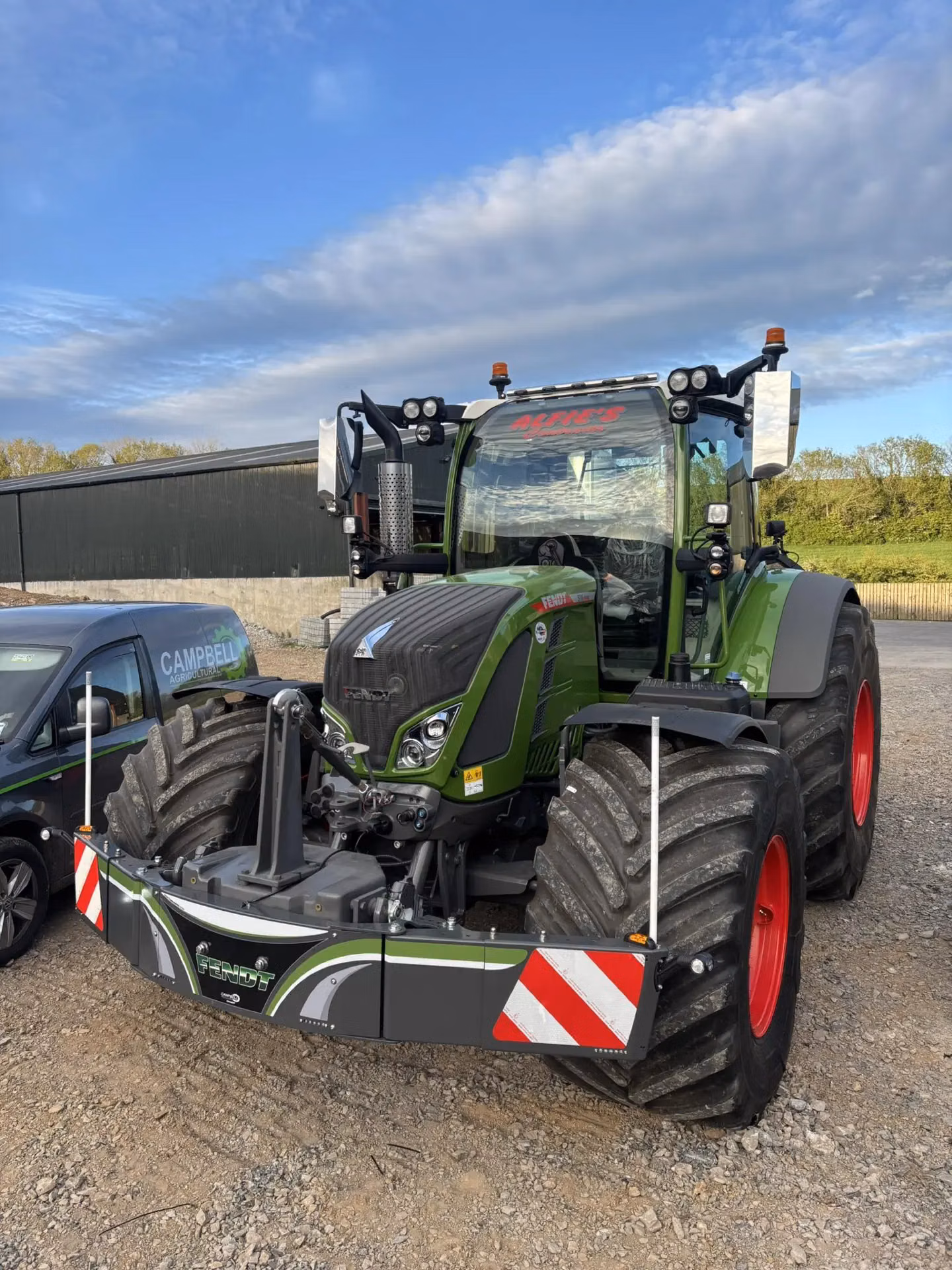 Large green tractor with a front weight bumper featuring lights, safety markings and reflective panels on a gravel lot