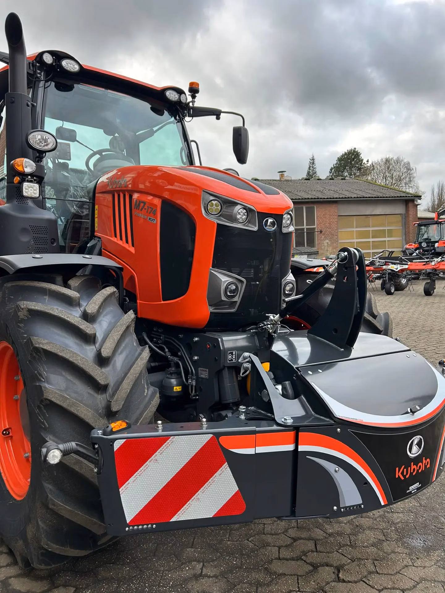 A large orange tractor fitted with a Kubota front weight bumper featuring red and white reflective stripes