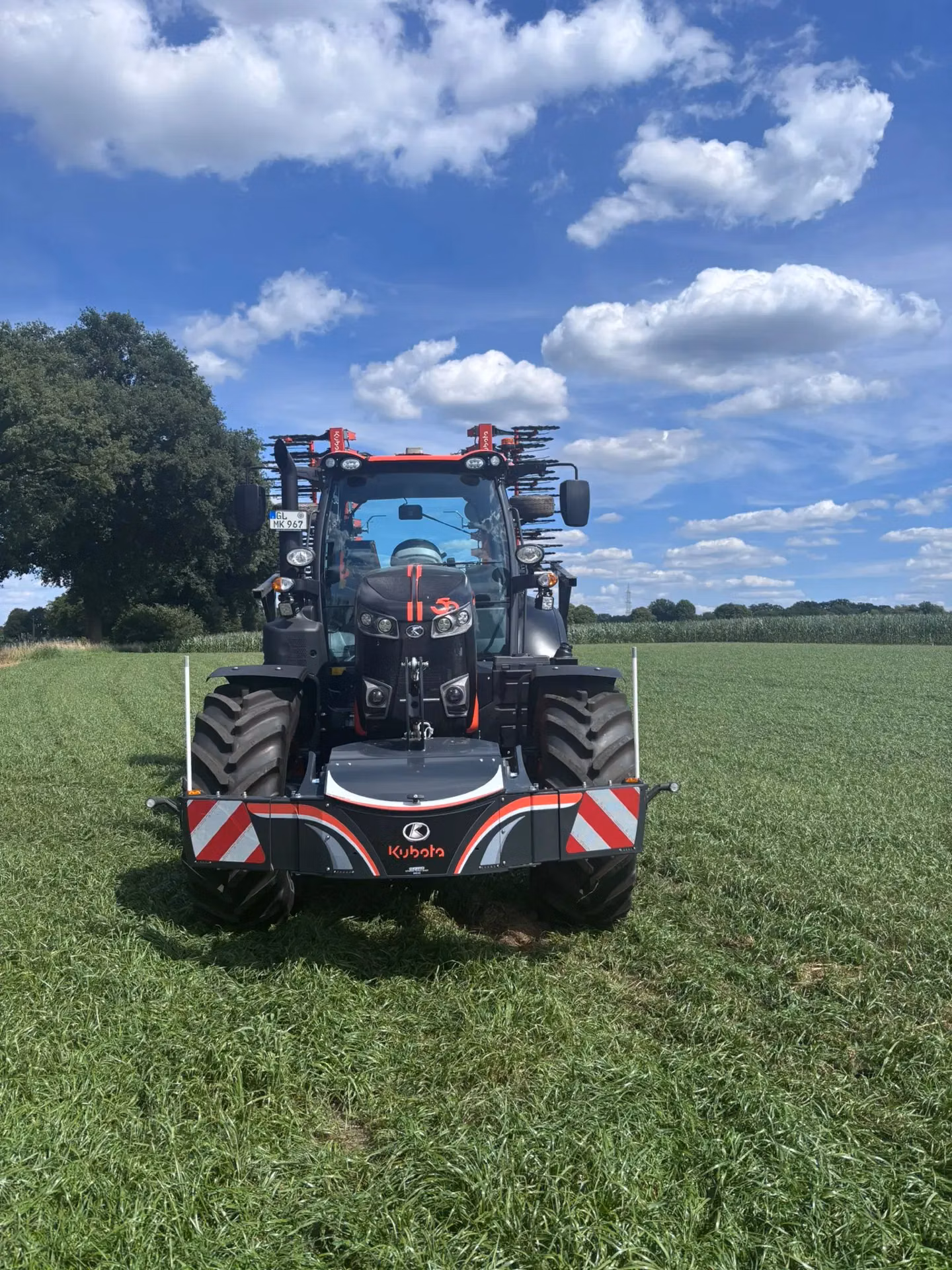 Tractor with a Kubota front weight bumper featuring red and white safety stripes parked on grass under a blue sky