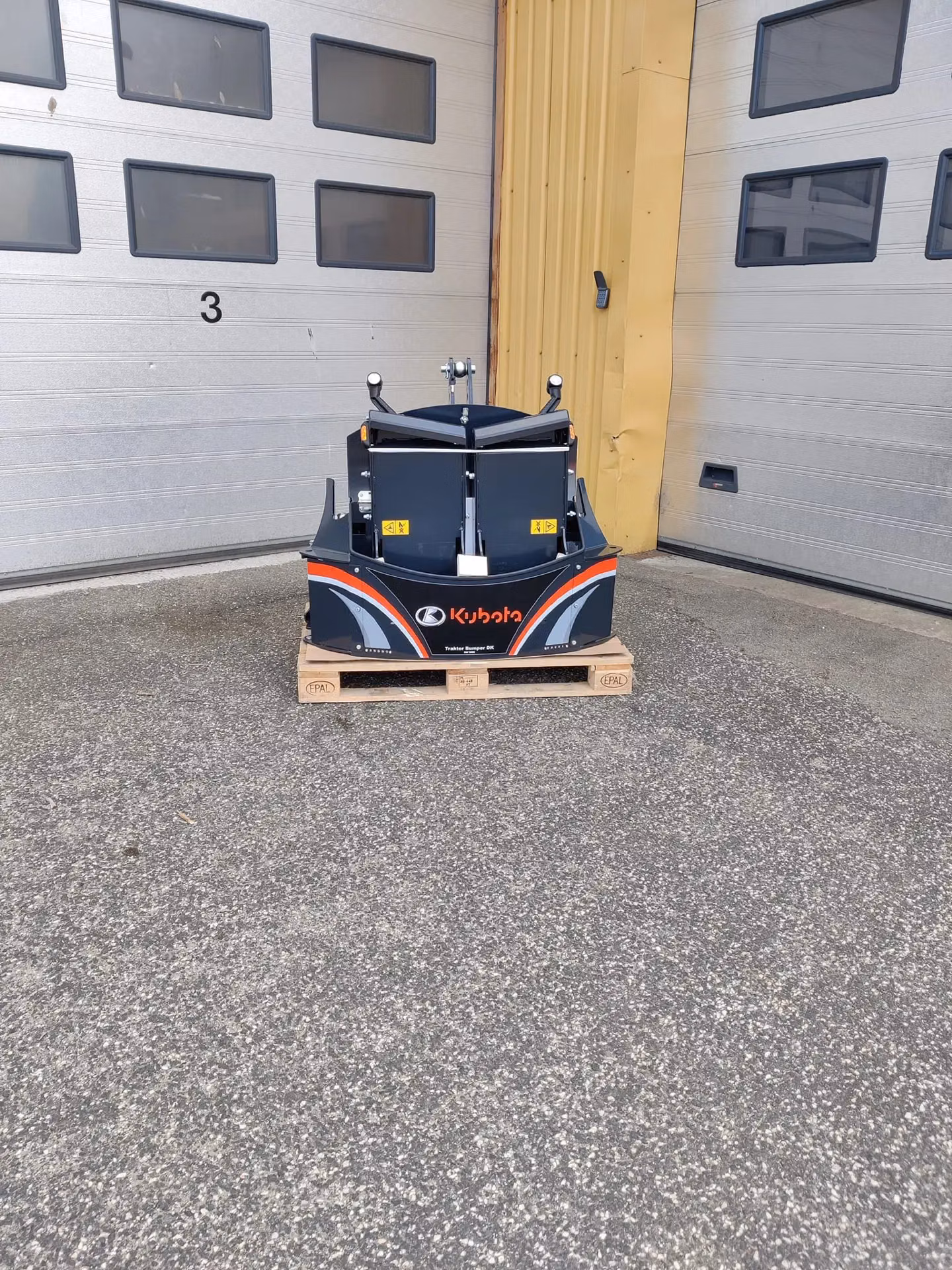 A Kubota front weight bumper for a tractor is displayed on a pallet in front of a garage door.