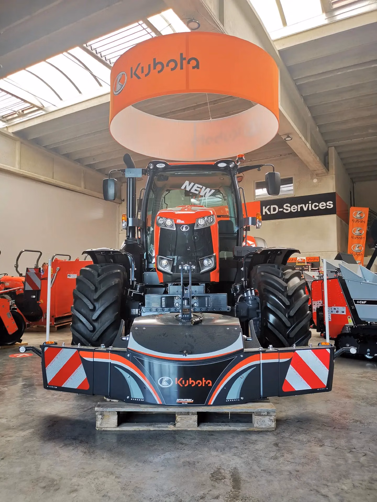 A front weight bumper with Kubota branding is mounted on a tractor displayed indoors on a wooden pallet